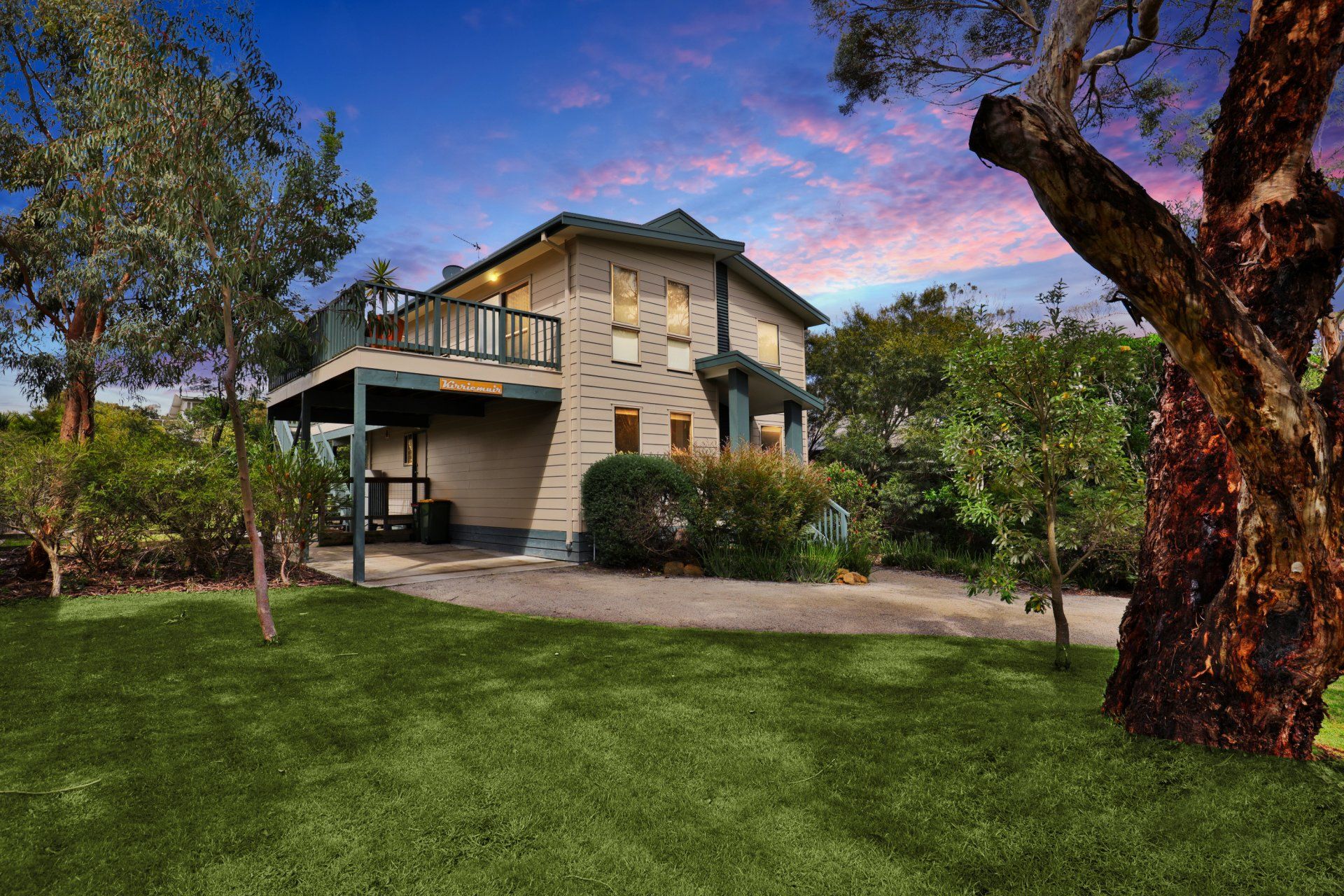 Two-story house with balcony and large green lawn under a blue sky