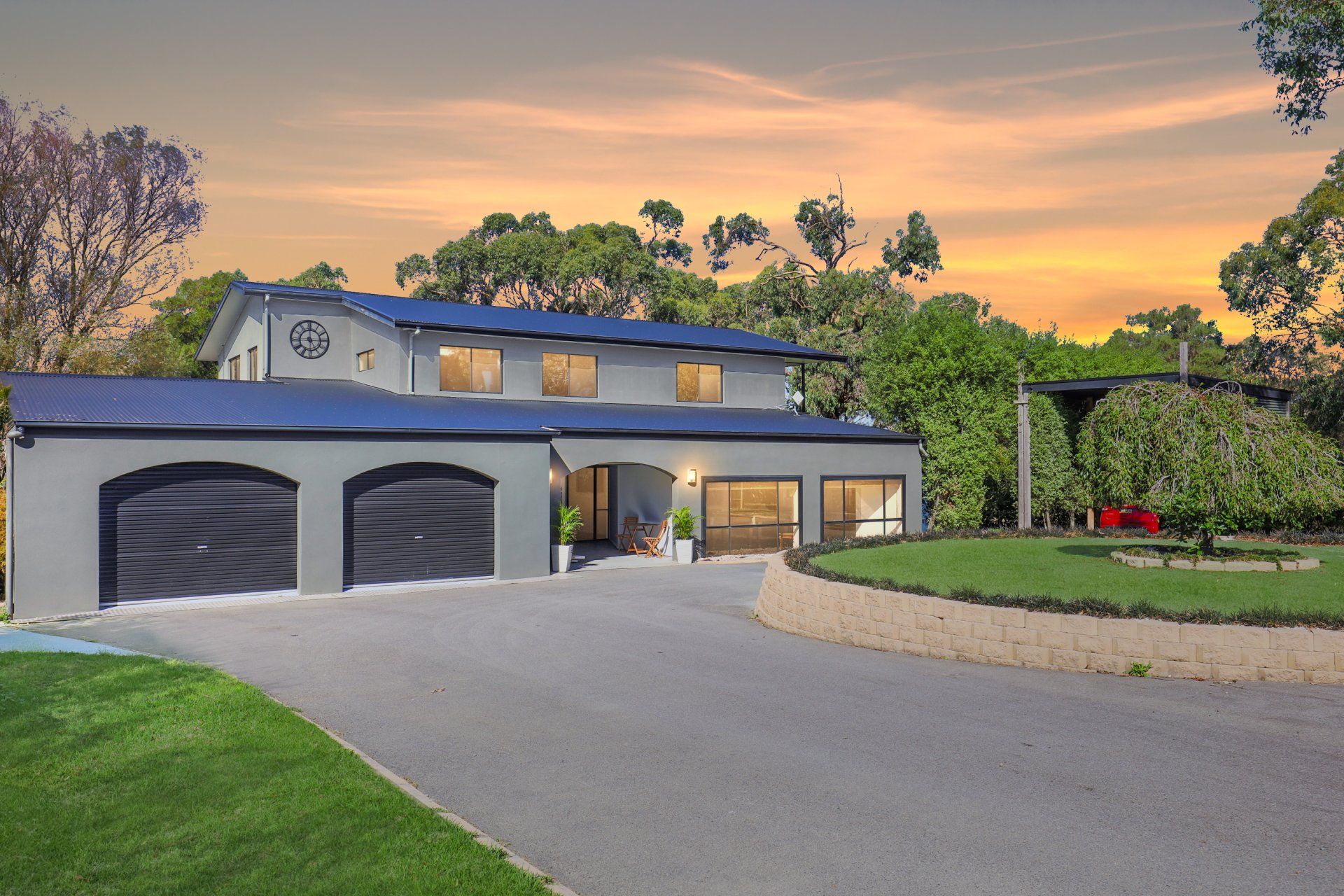 Modern two-story house with three-car garage, curved driveway, and landscaped yard at sunset
