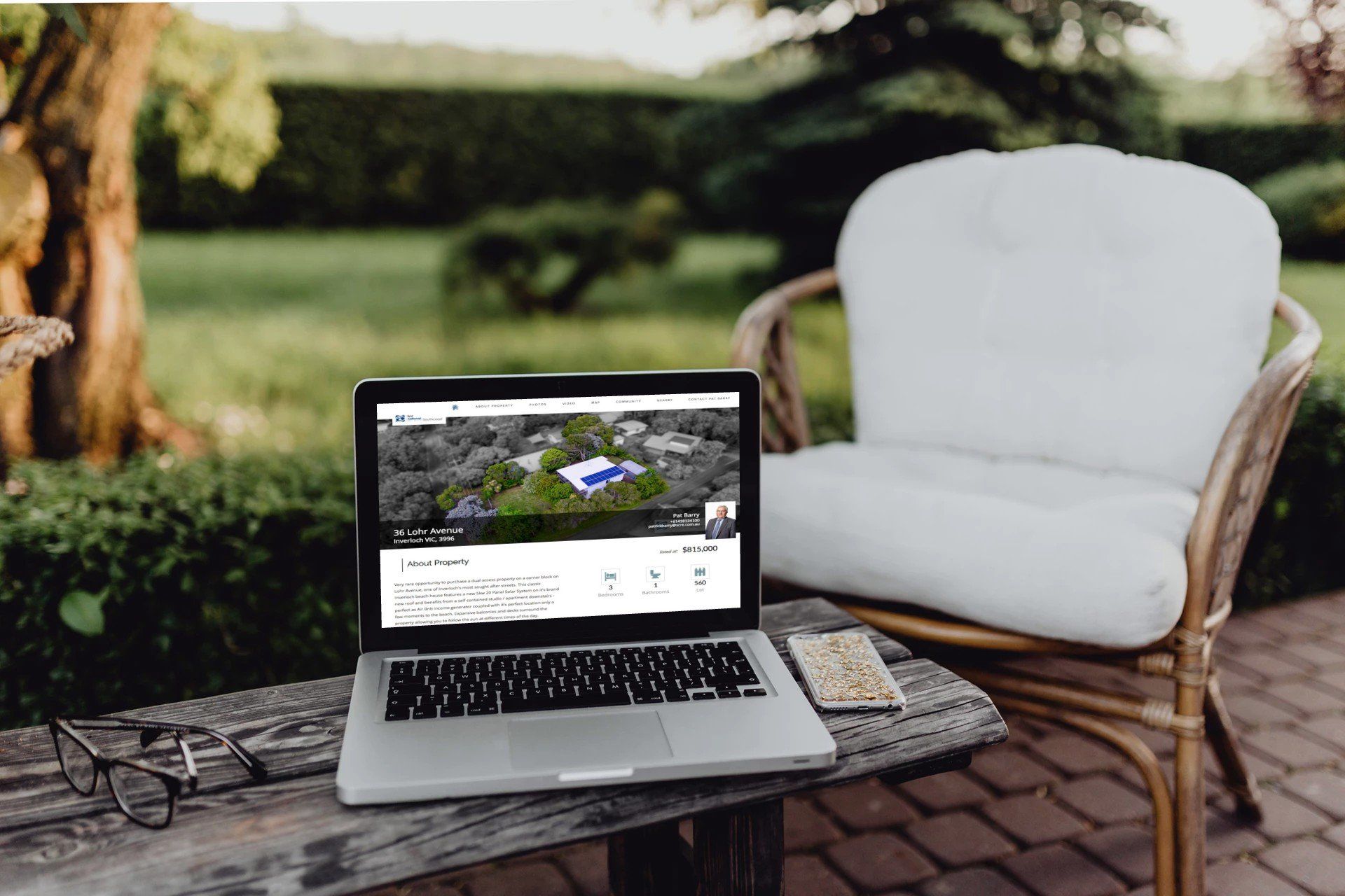 Silver laptop on a wicker chair beside a white cushion outdoors in a garden patio.