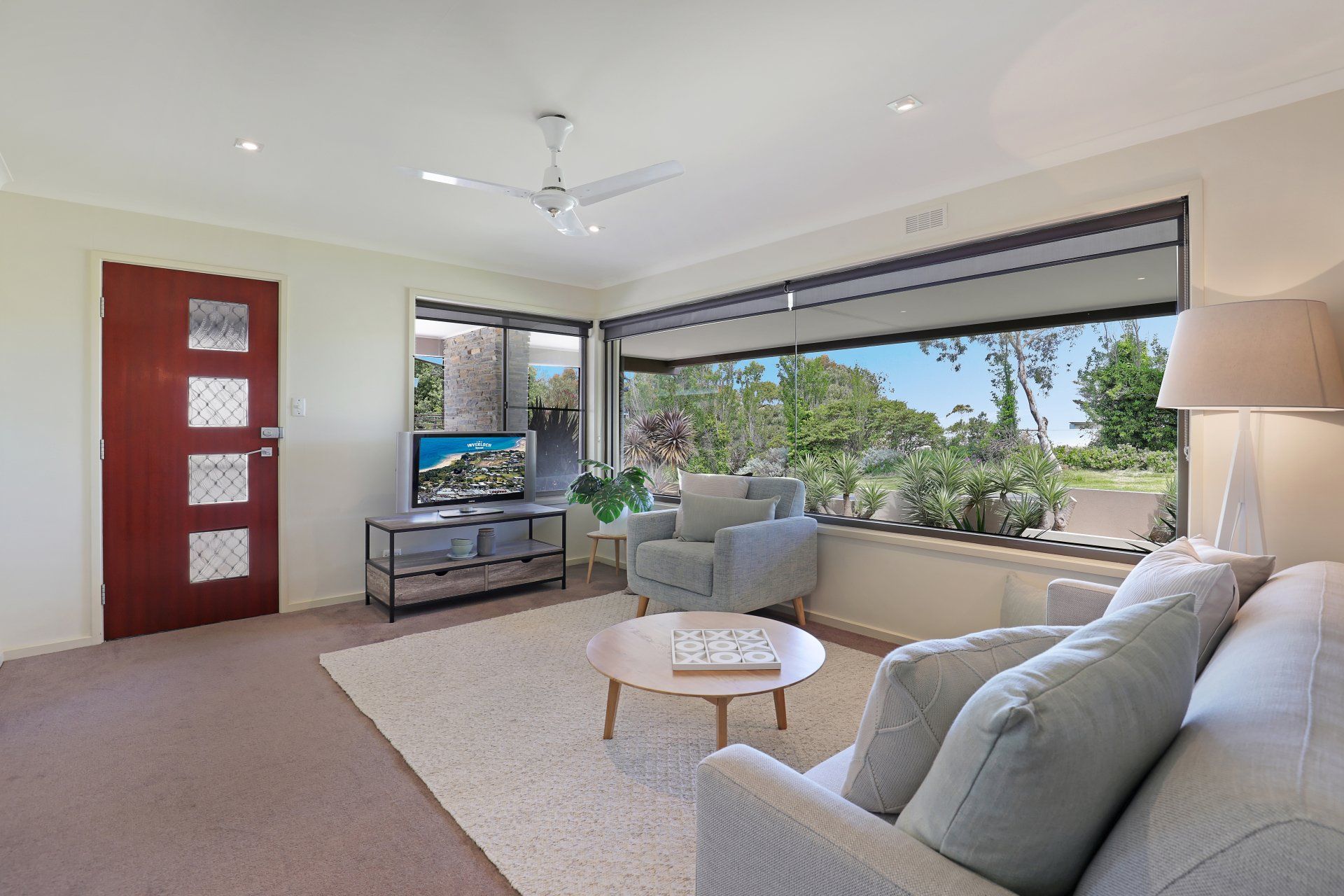 Bright living room with gray sofa, red door, and large windows overlooking greenery