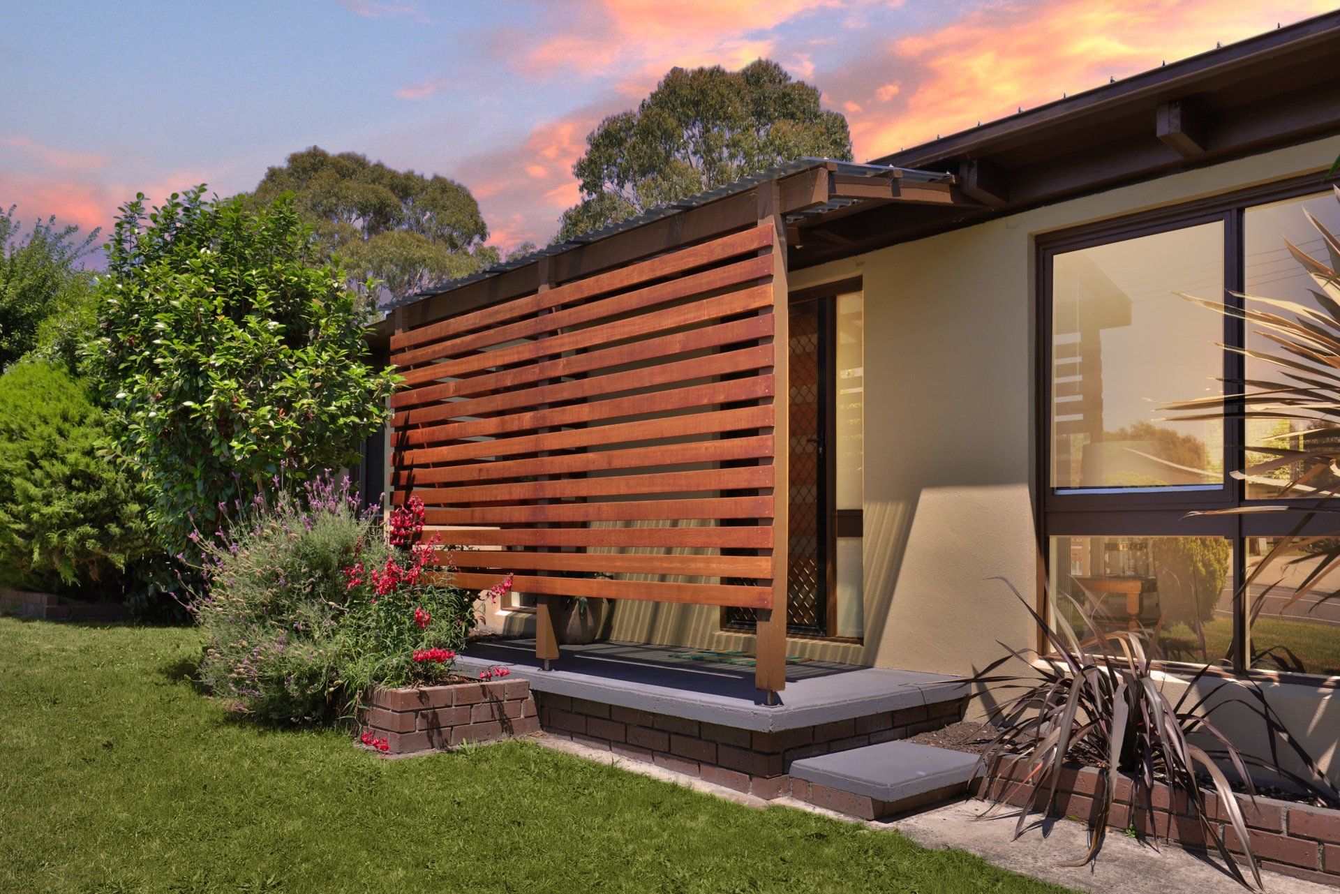 Modern house patio with wooden slat screen, steps, garden, and sunset sky
