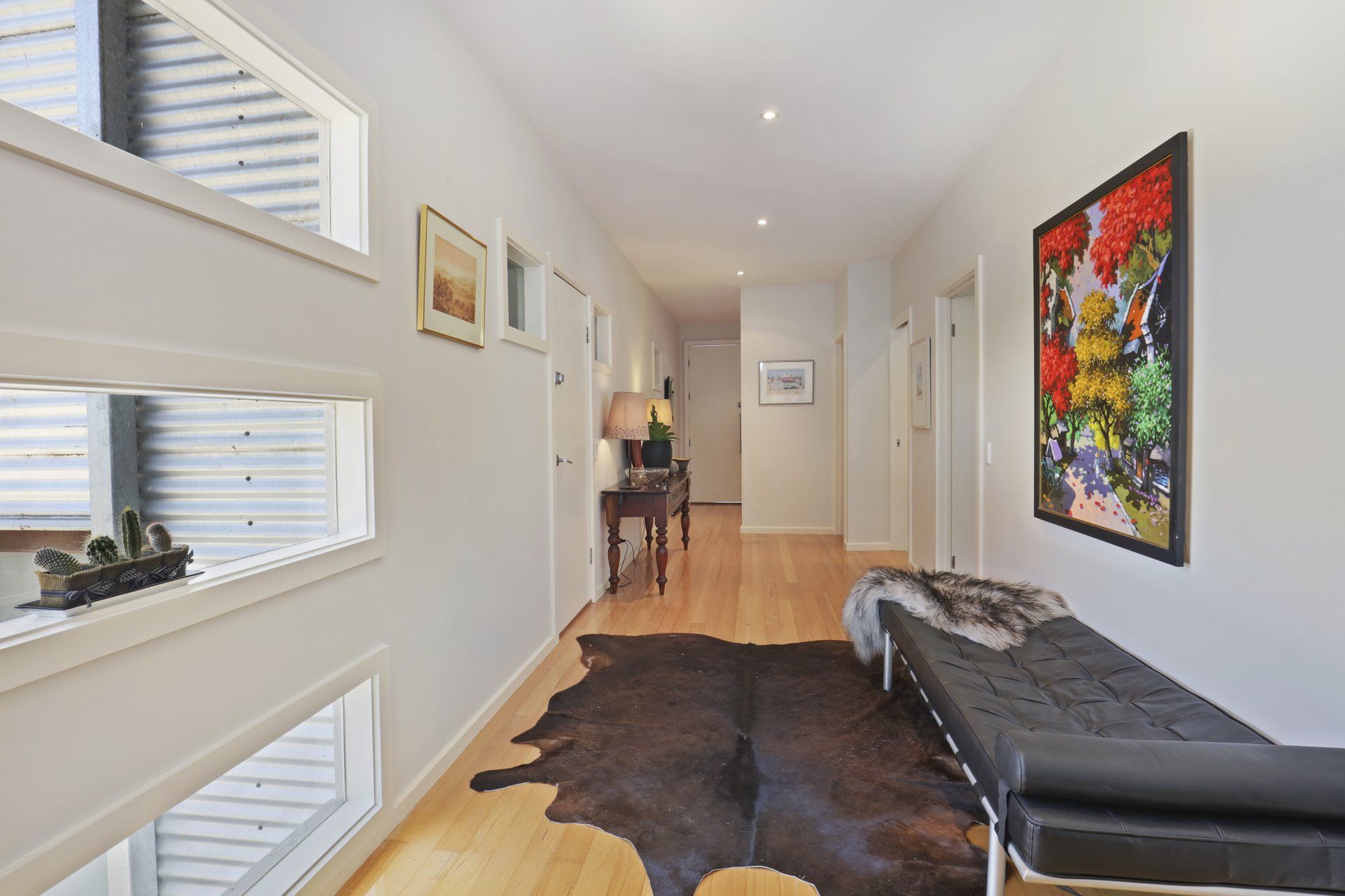 Bright hallway with hardwood floors, black bench, cowhide rug, and colorful wall art.