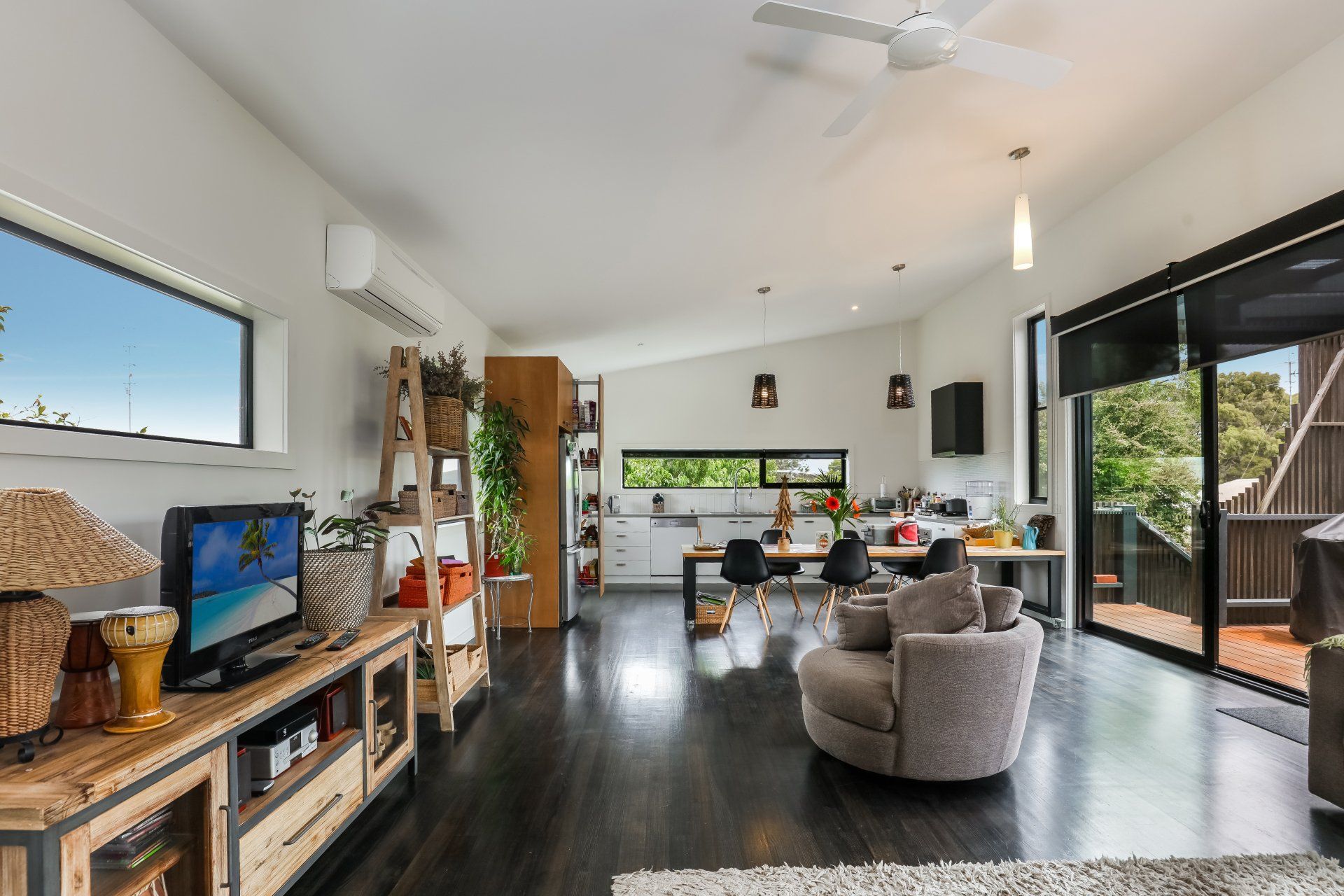 Bright modern living room with dark floors, gray chairs, TV, and large sliding glass doors to a deck