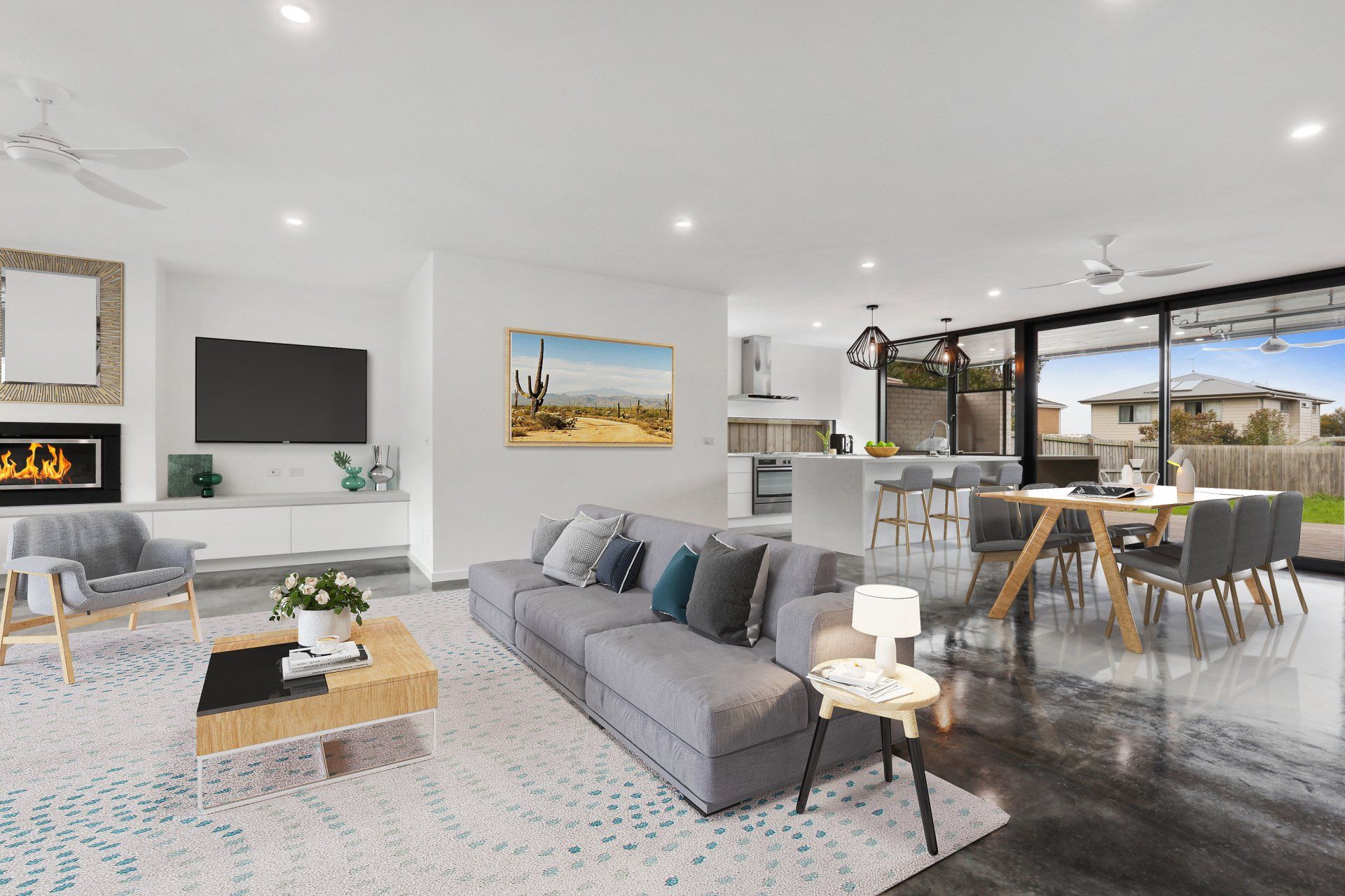 Modern open-plan living room with gray sofas, wall TV, dining area, and large windows to a patio