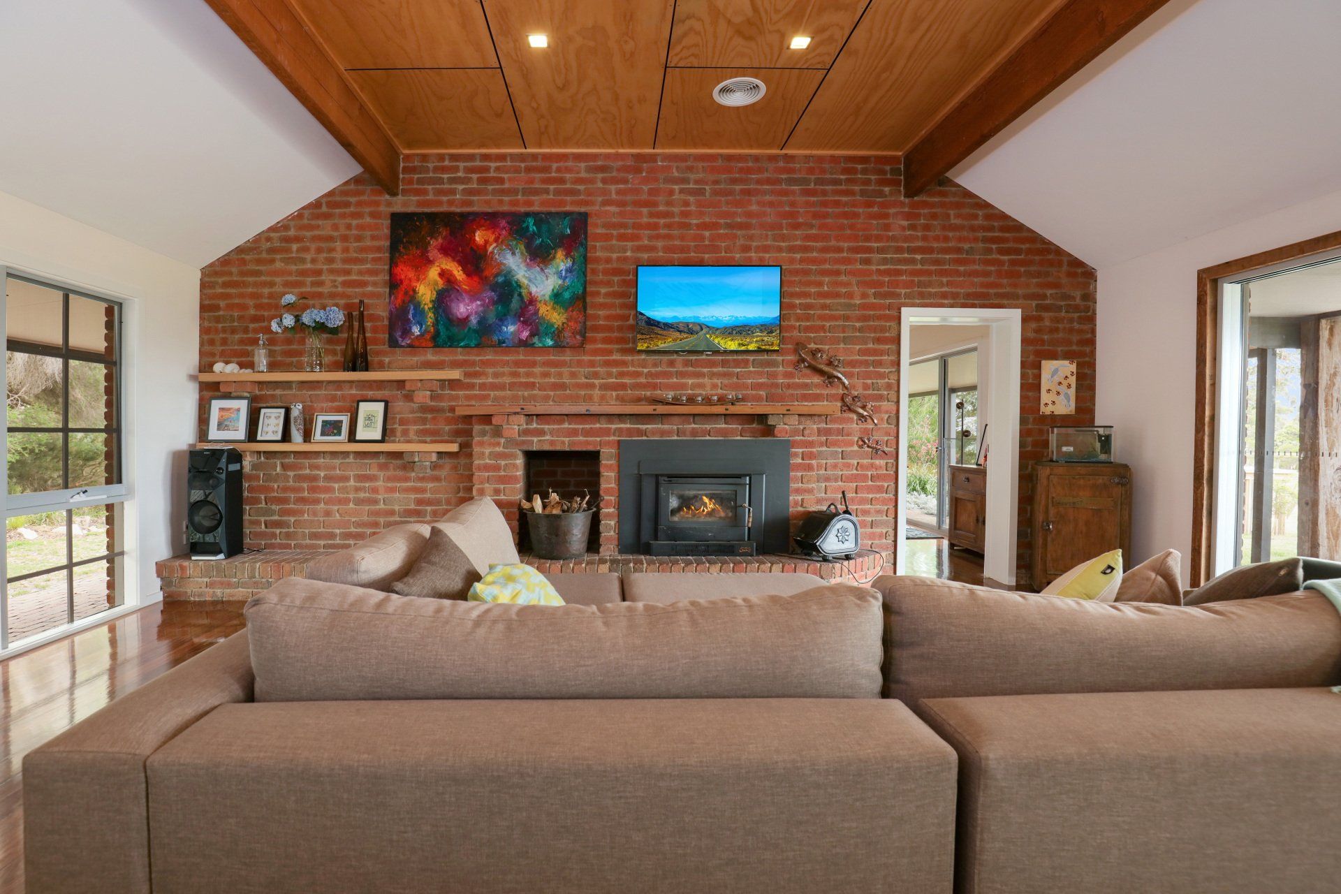 Cozy living room with brick fireplace, wall-mounted TV, and brown sectional sofa under a wood ceiling