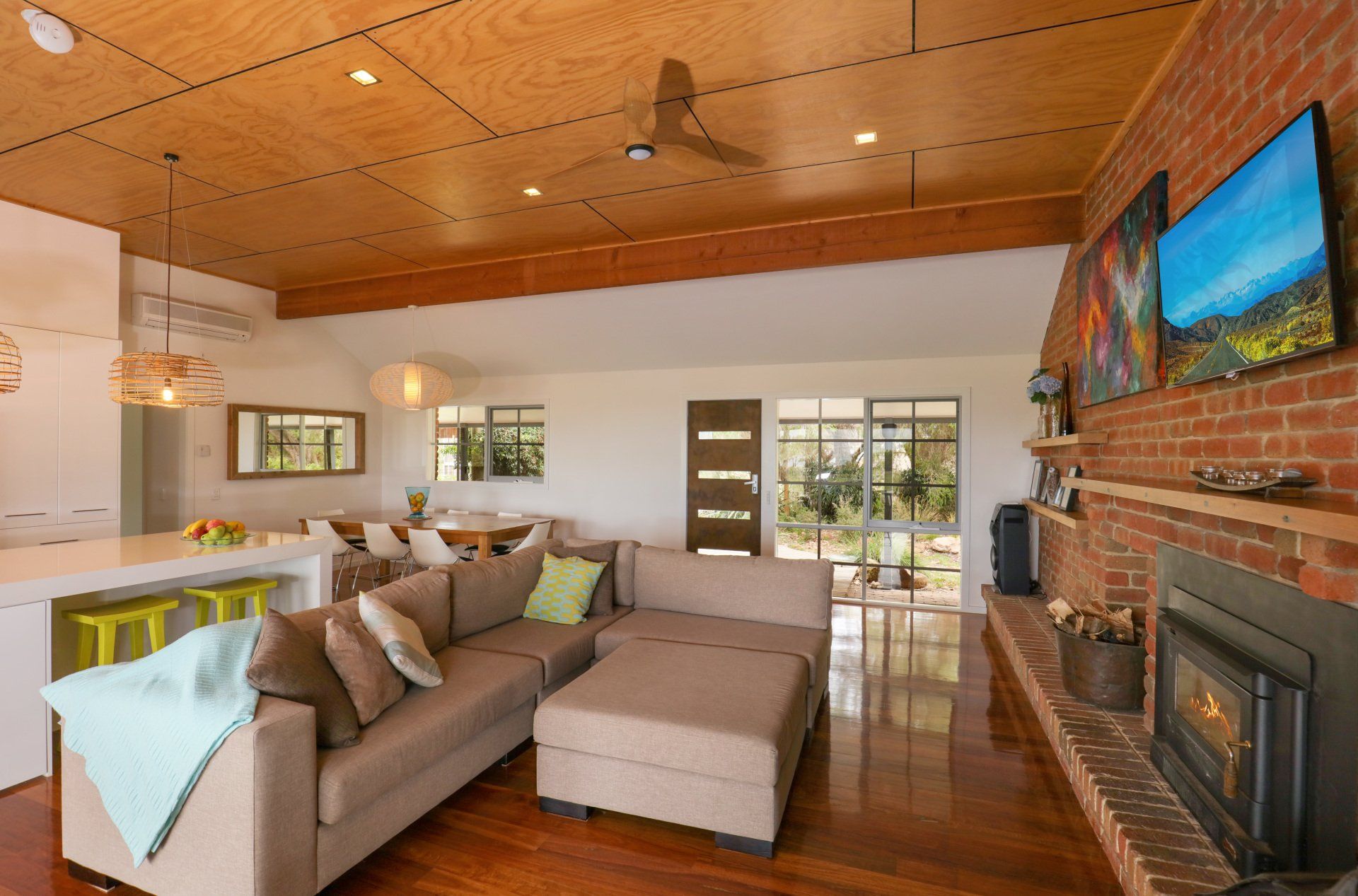Bright living room with sectional sofa, brick fireplace, wood ceiling, and wall-mounted TV