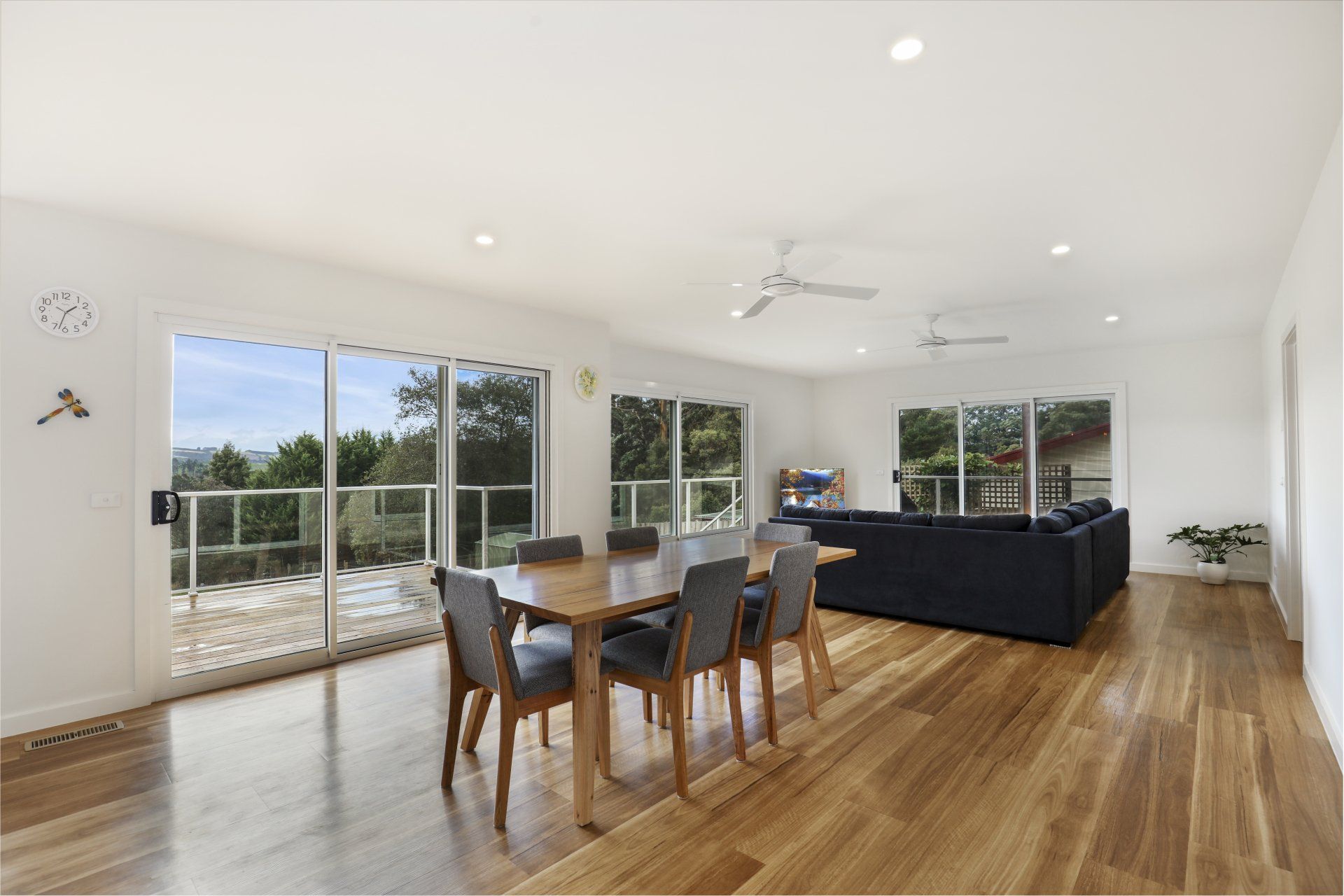 Bright open living-dining room with hardwood floors, large windows, and a dark sofa.
