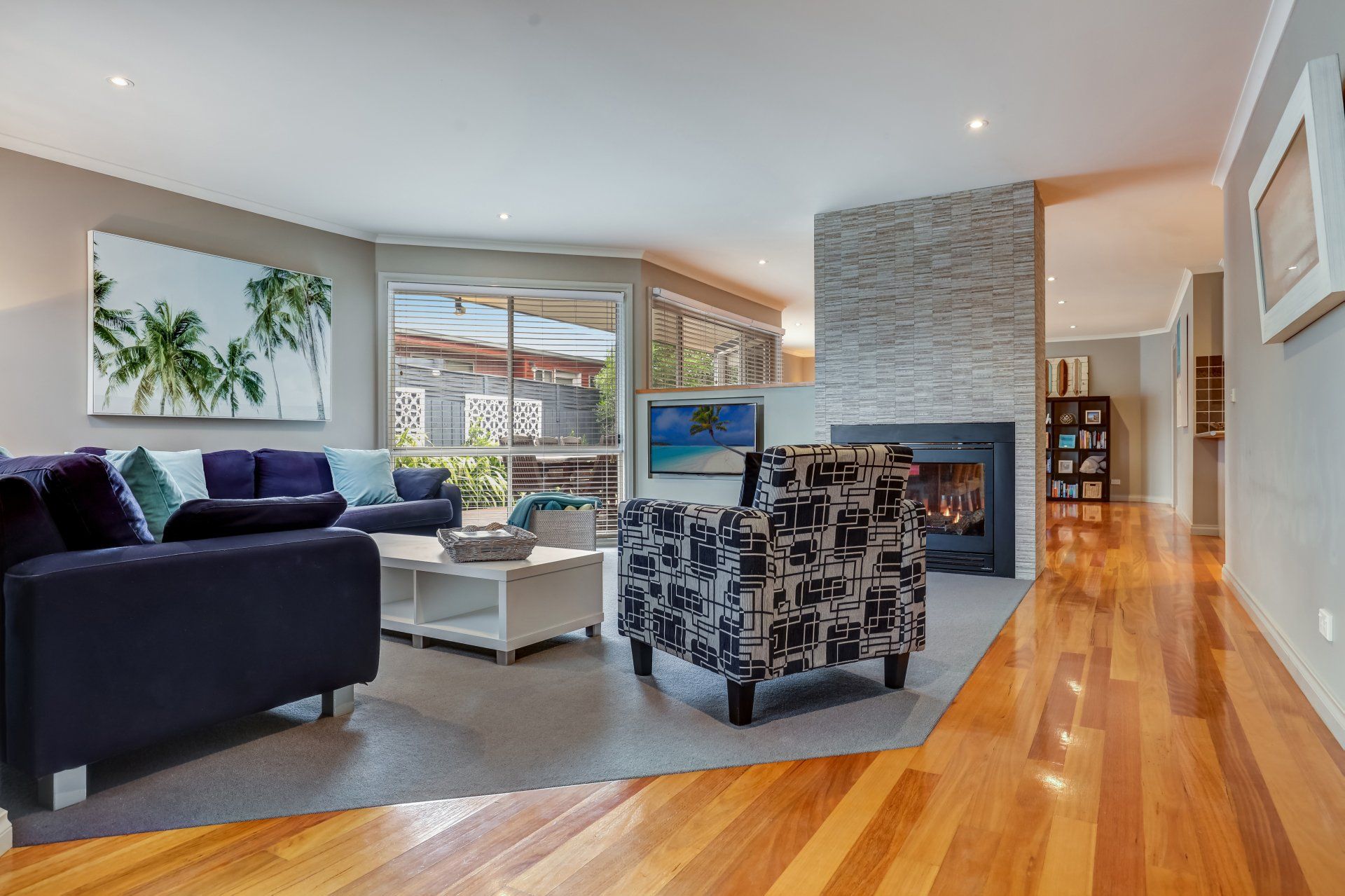 Bright modern living room with sectional sofa, stone fireplace, wood floors, and large windows