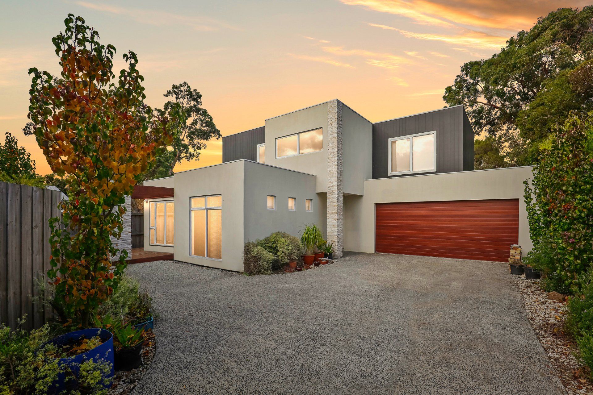 Modern two-story house with gravel driveway, wood garage door, and sunset sky