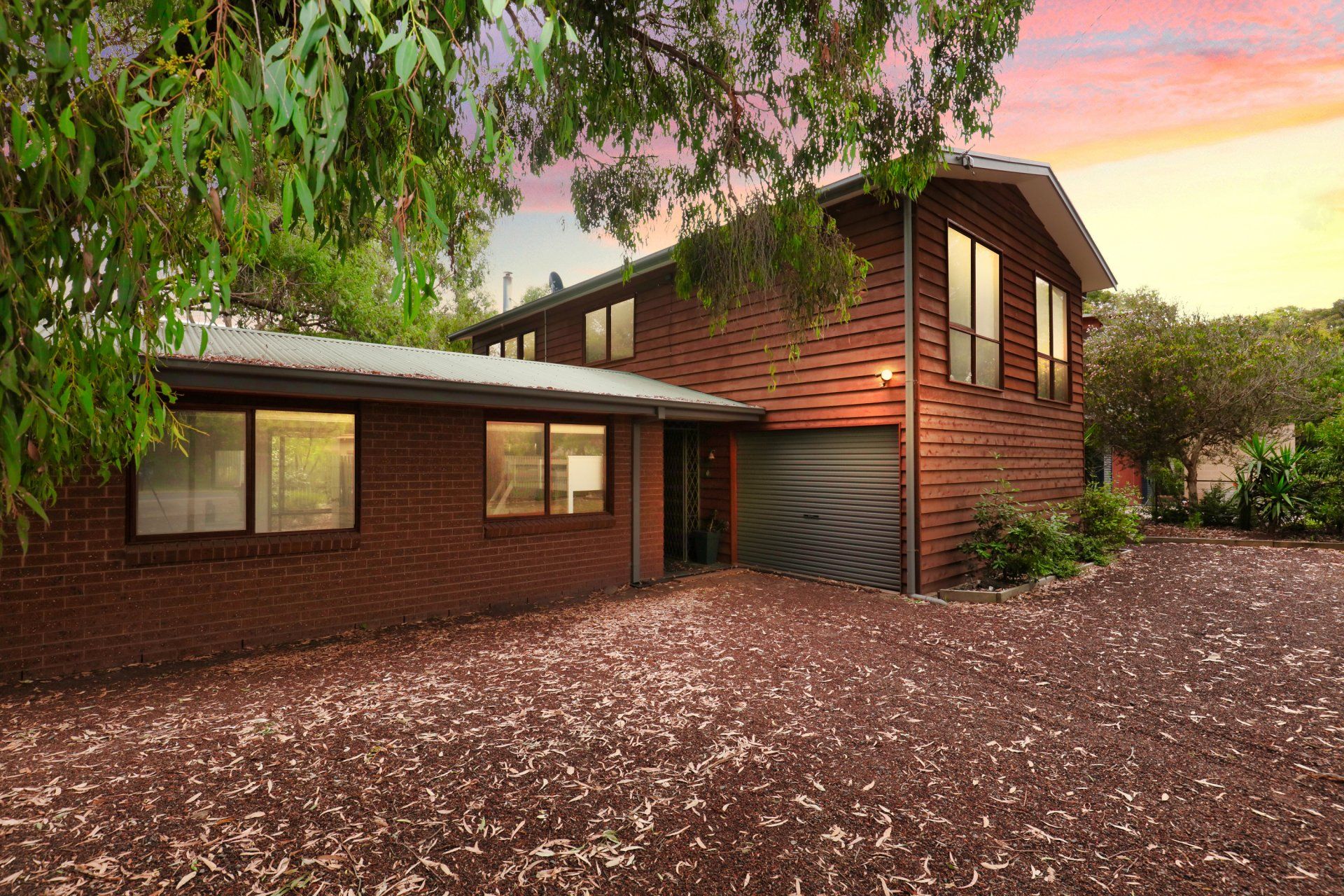Modern two-story brick house with wood siding, garage, and a leaf-covered yard at sunset