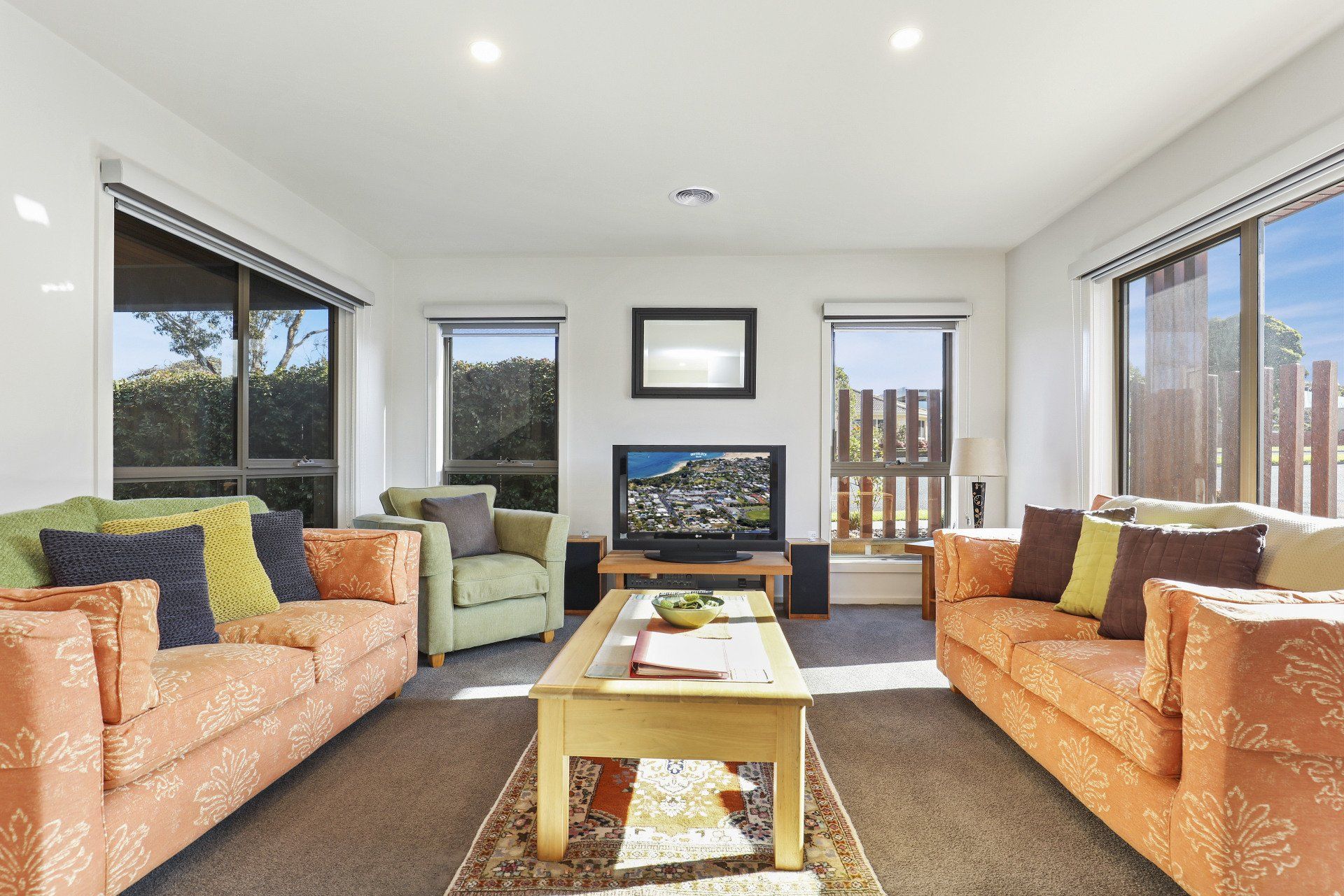 Bright living room with two orange sofas, a TV, coffee table, and large windows with a balcony view