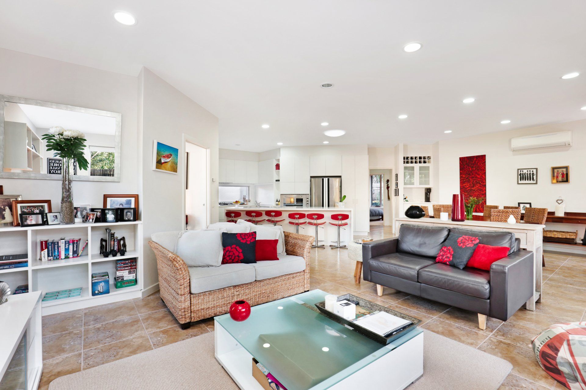 Bright, open living room with white walls, gray sofas, red accents, and a kitchen bar in the background