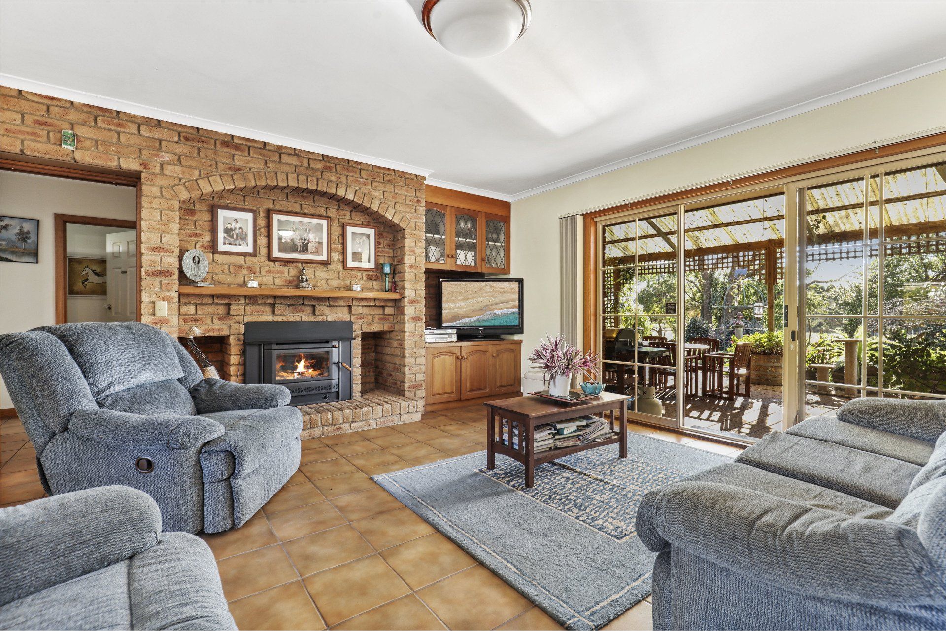 Cozy living room with brick fireplace, gray sofas, rug, coffee table, and sliding glass doors to a patio