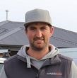 Man wearing a gray cap and hoodie, standing in front of a house roof, looking at the camera.