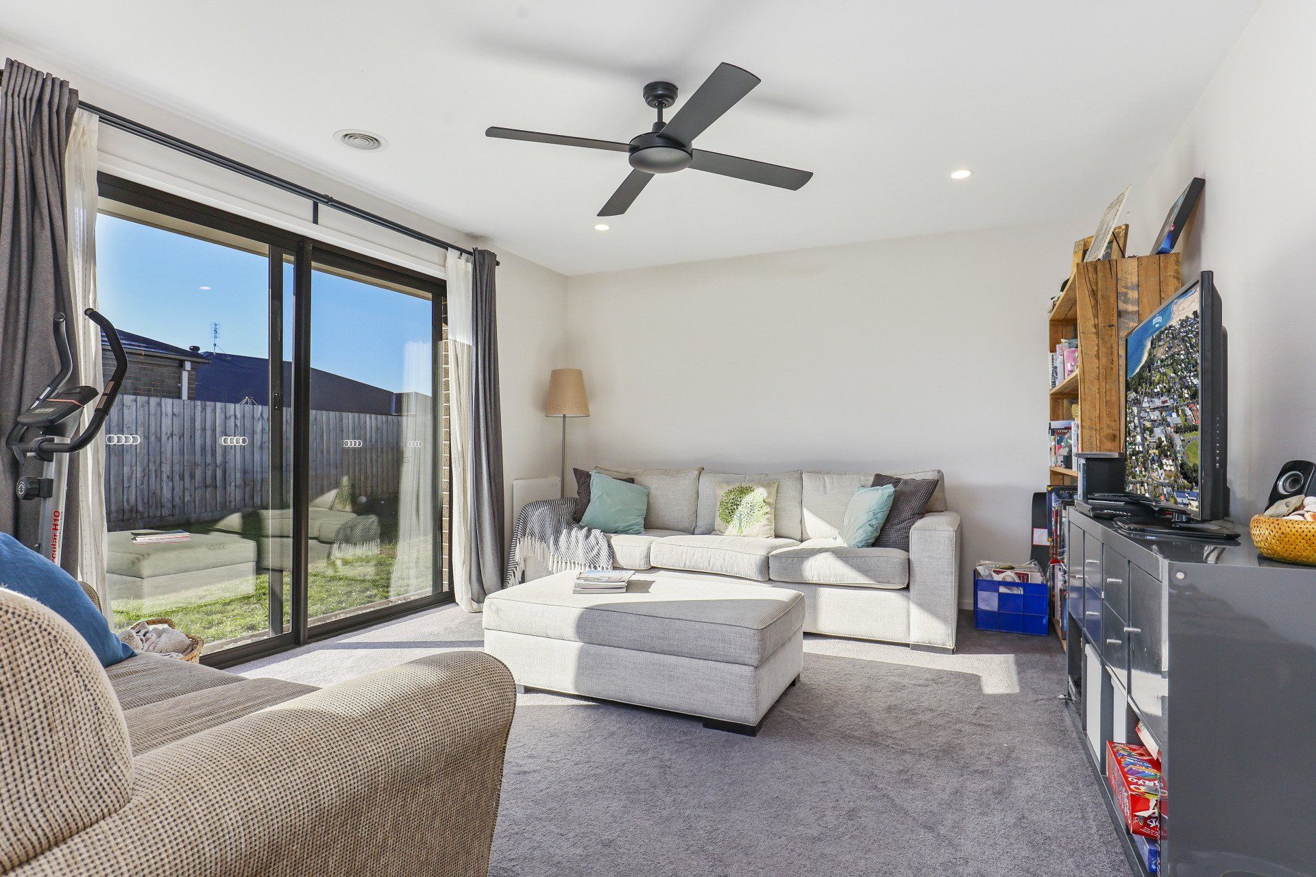 Bright living room with gray sectional, ottoman, large sliding glass doors, and ceiling fan.