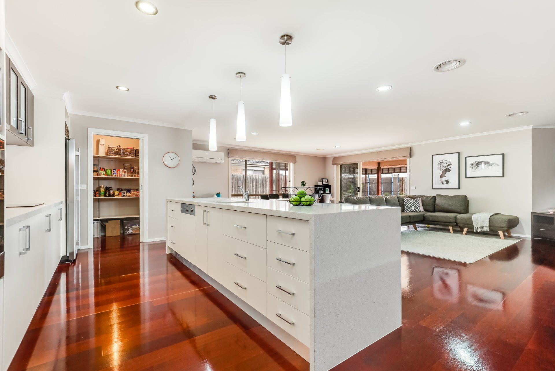 Modern open-plan kitchen with white island, polished wood floors, and a living area in the background