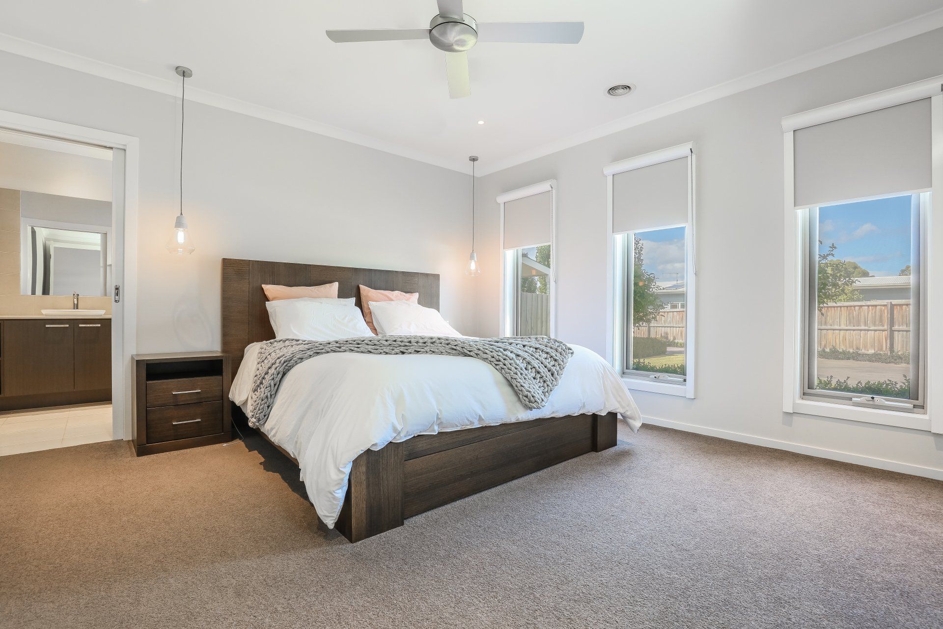 Bright bedroom with a bed, nightstand, carpet, and three windows letting in natural light.