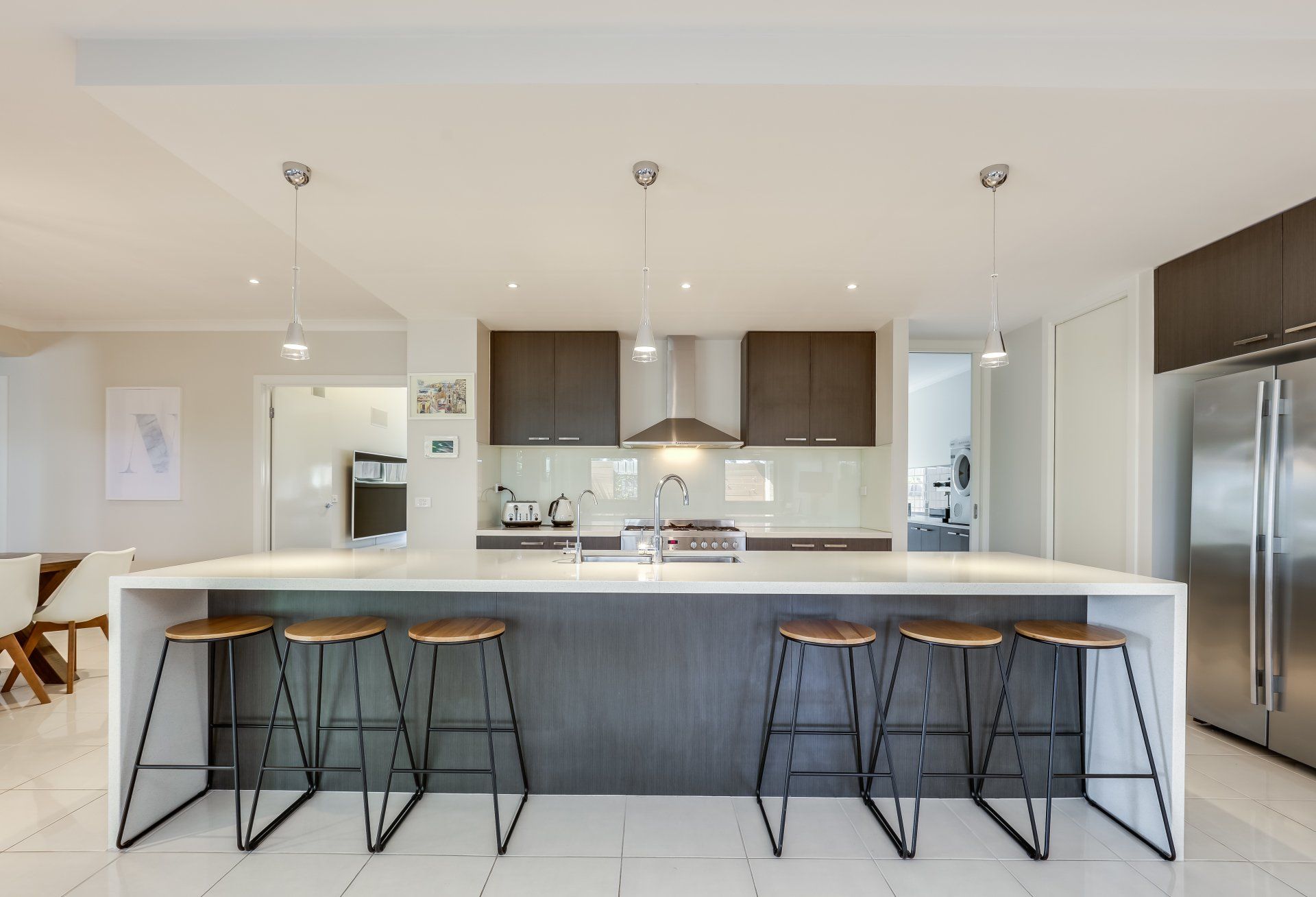 Modern kitchen with large island, pendant lights, dark cabinets, and bar stools