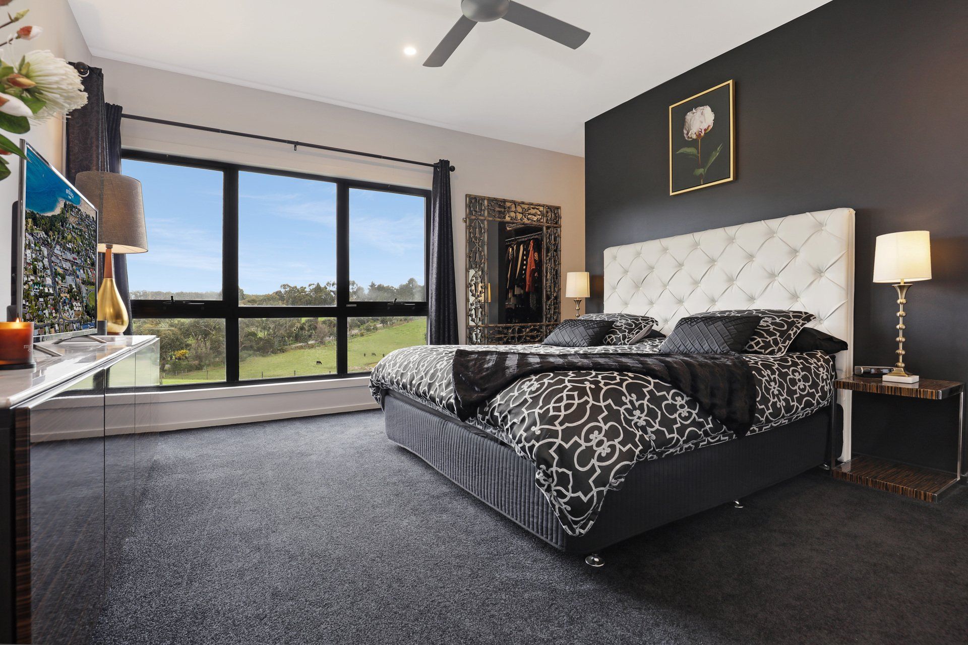 Modern bedroom with dark walls, tufted bed, large windows, and a countryside view