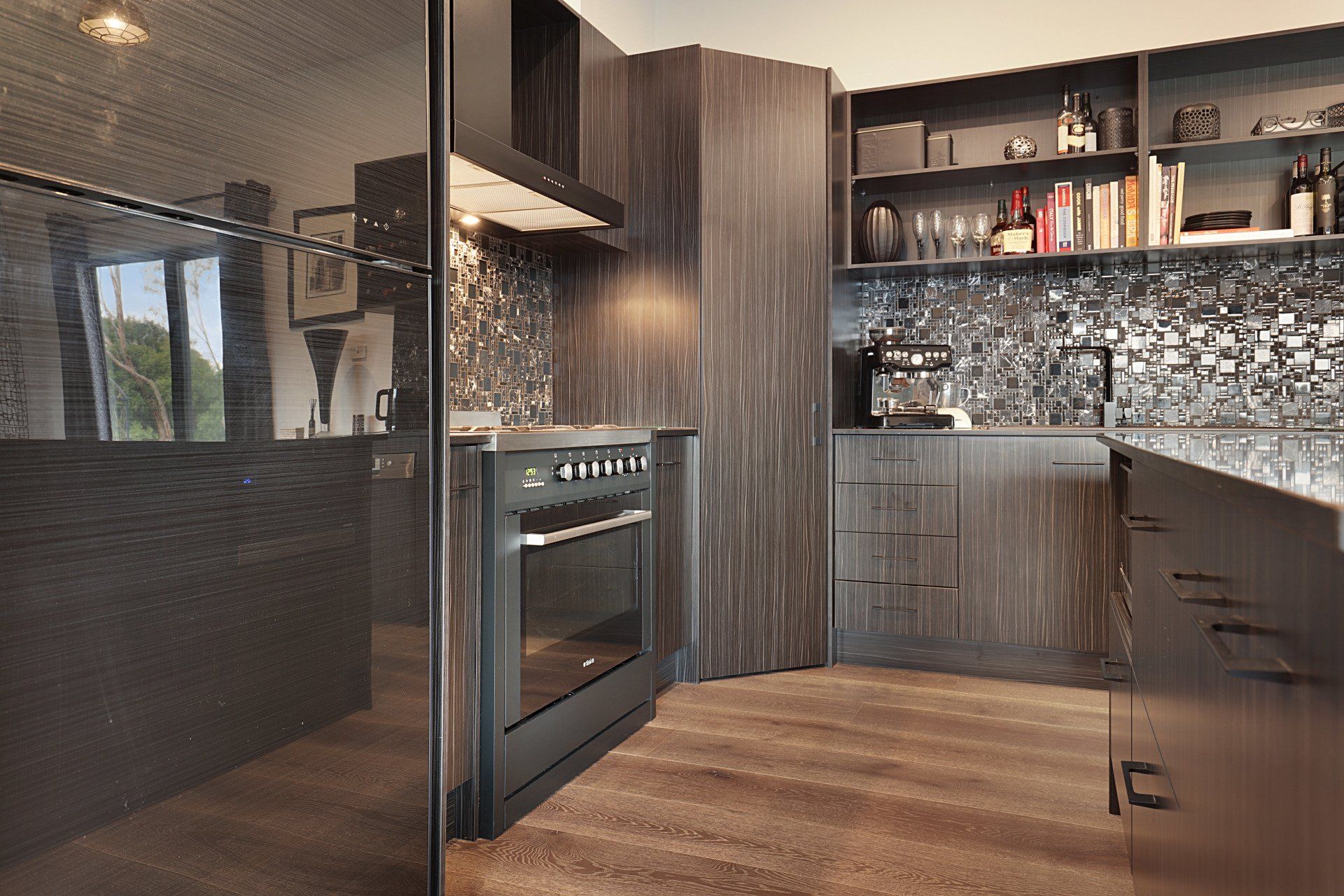 Modern kitchen with dark wood cabinets, stainless oven, mosaic backsplash, and wood floor