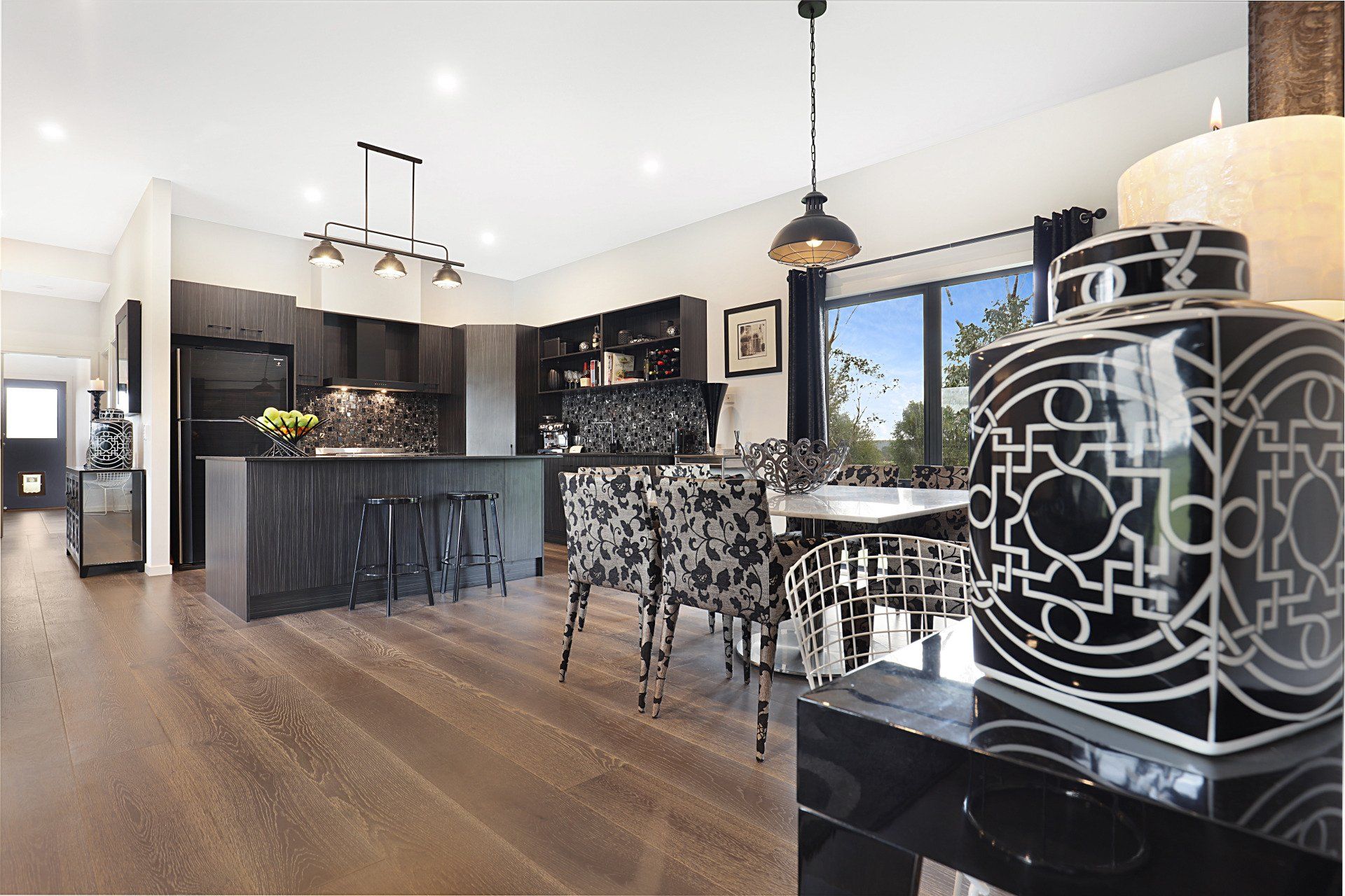 Modern black-and-white kitchen and dining area with island, patterned chairs, wood floors, and large window