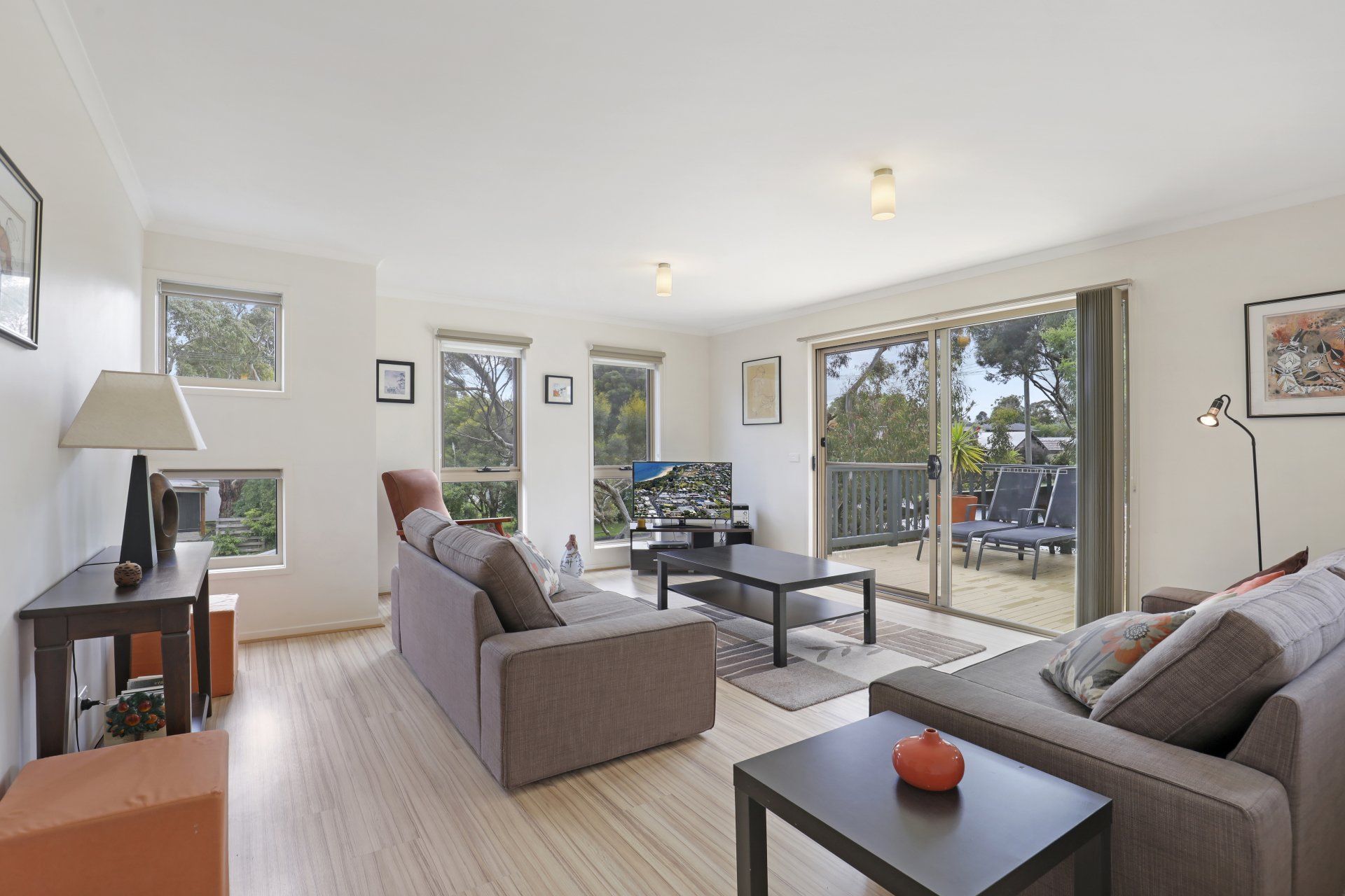 Bright modern living room with gray sofas, large windows, and a sliding door opening to a patio and trees.