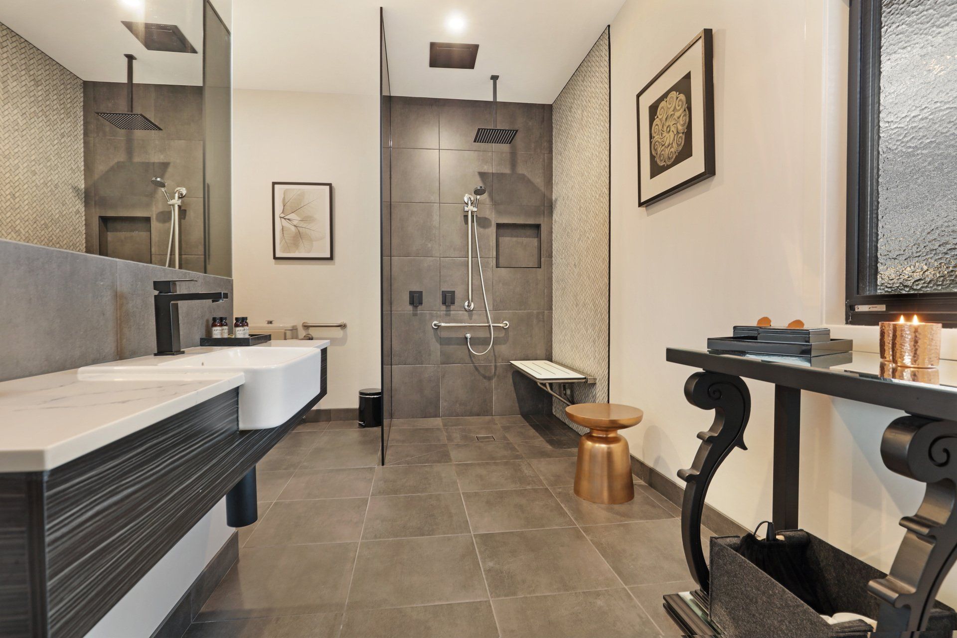 Modern bathroom with double sinks, large shower, gray tile, and a black vanity table with candles.