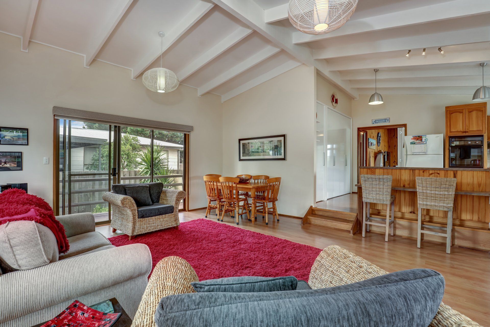 Bright open living room with striped sofa, red throw, dining area, and kitchen counter in the background