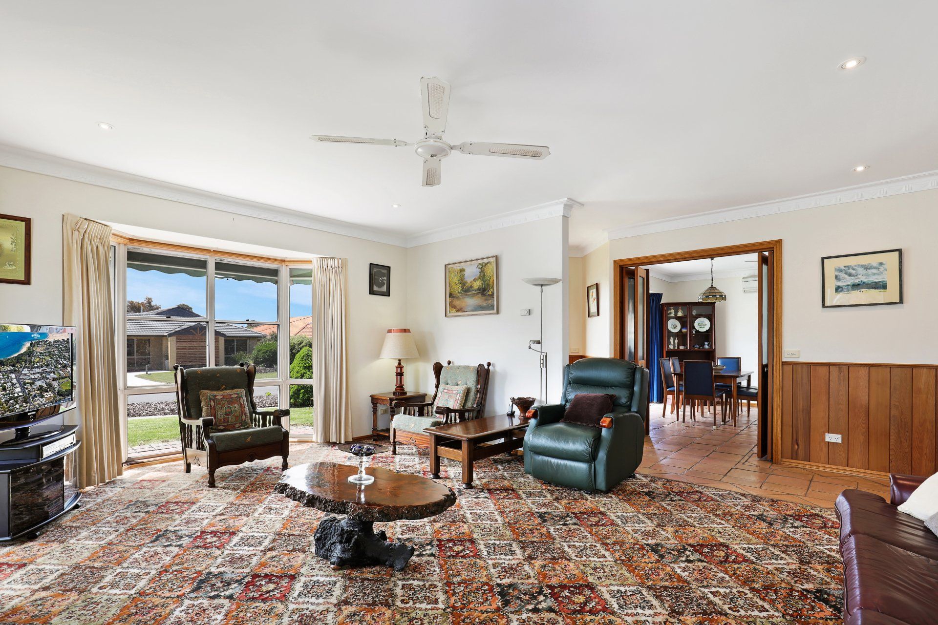 Bright living room with patterned rug, leather chairs, dining area, and sliding doors to a sunny patio