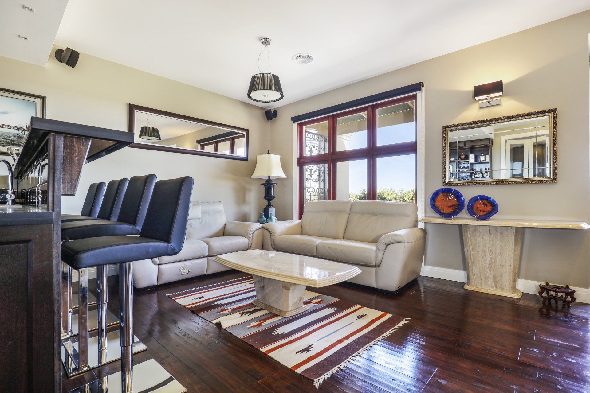 Modern living room with beige sofa, blue chairs, dark wood floor, and large windows.