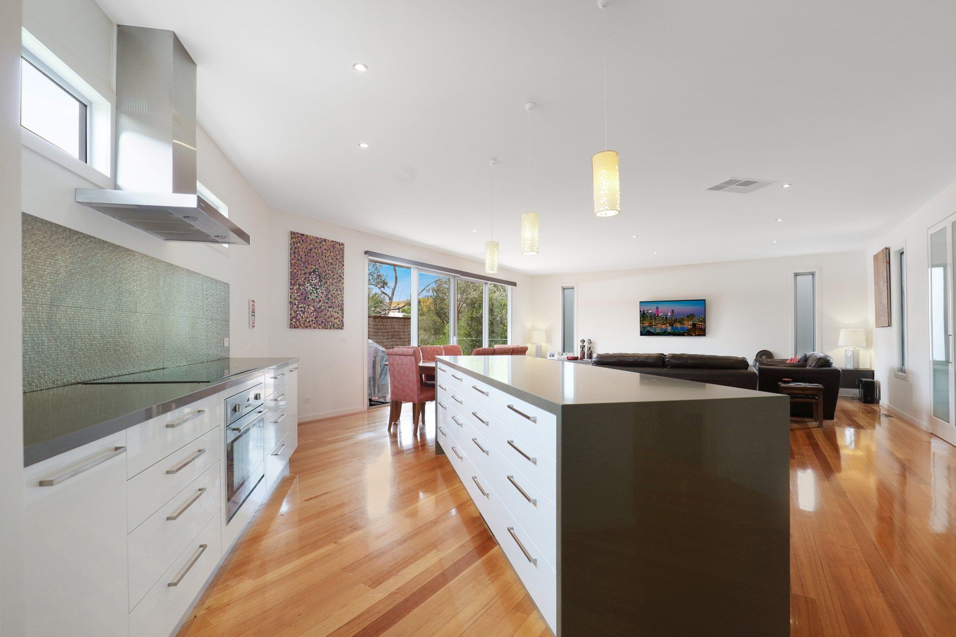 Modern open-concept kitchen and living room with white cabinets, wood floors, and large windows.