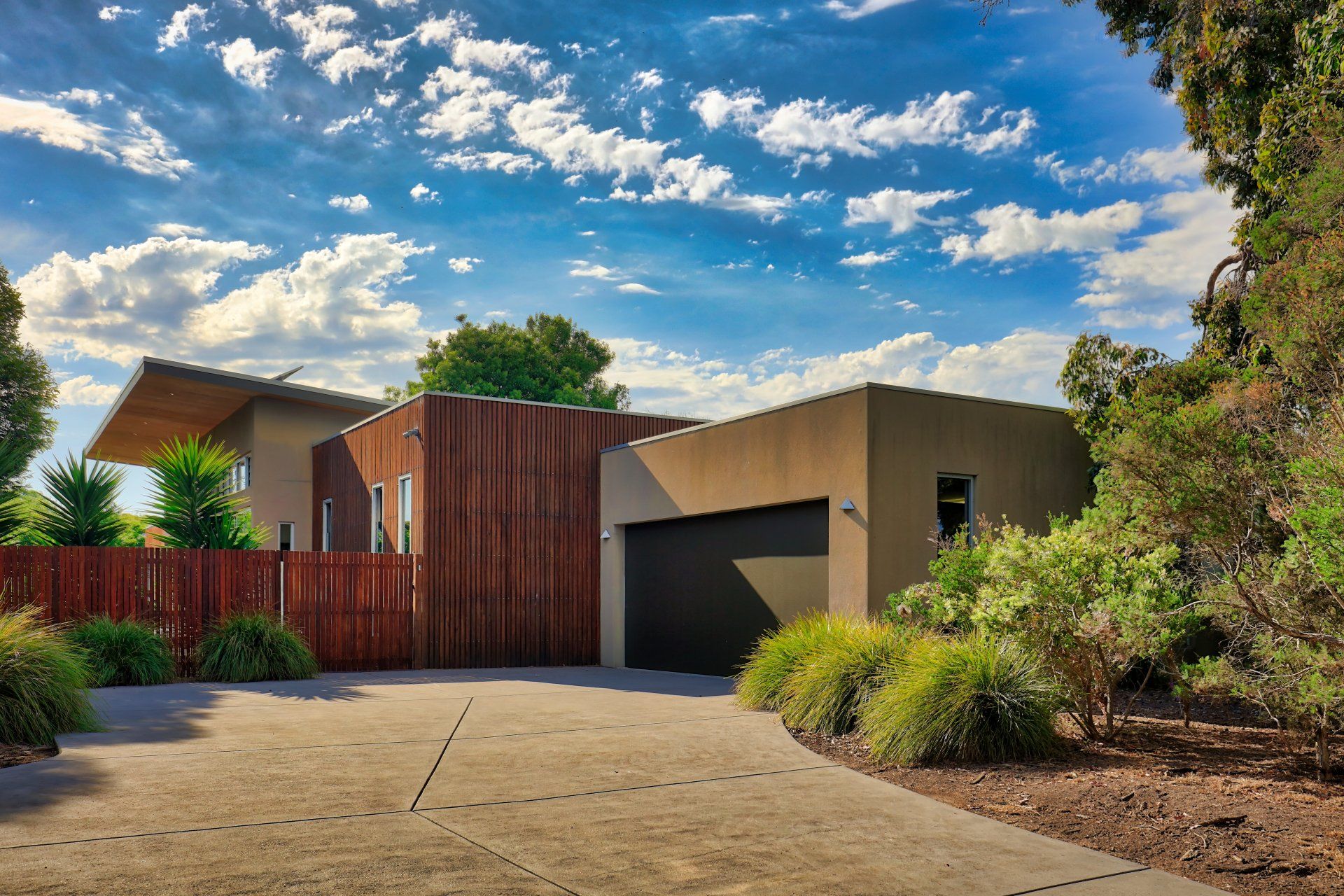Modern house exterior with a wooden gate, tan garage, and desert landscaping under a blue sky