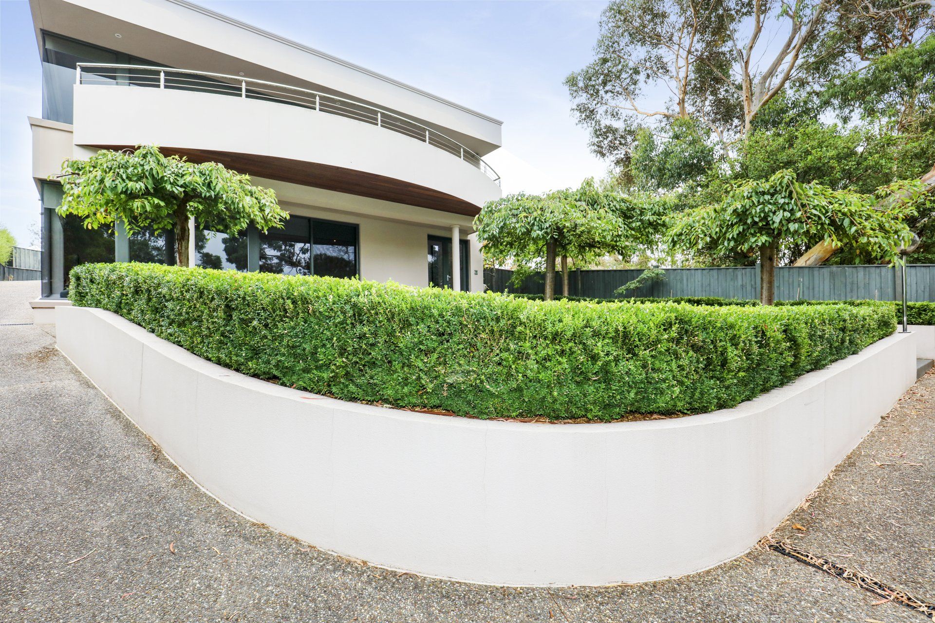 Curved white planter with green hedges beside a modern building and gravel path