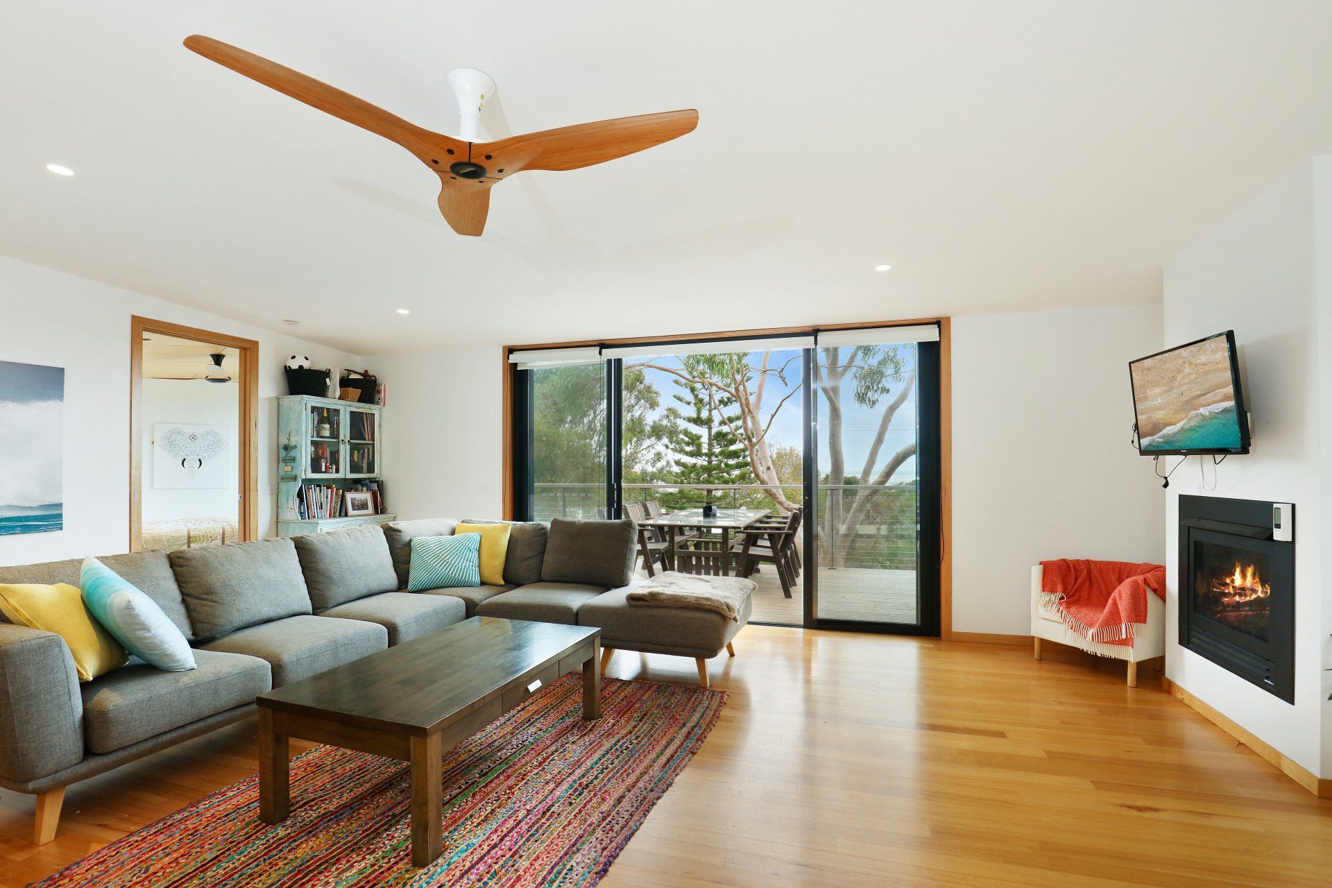 Modern living room with gray sectional, wood ceiling fan, fireplace, and large sliding doors to a deck.