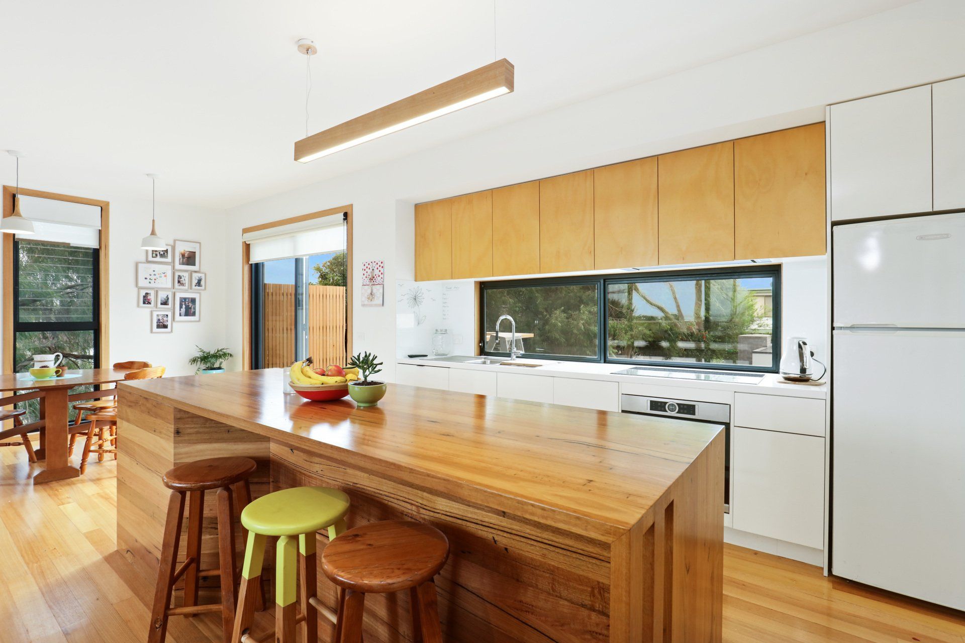 Bright modern kitchen with wooden island, stools, white appliances, and large window view