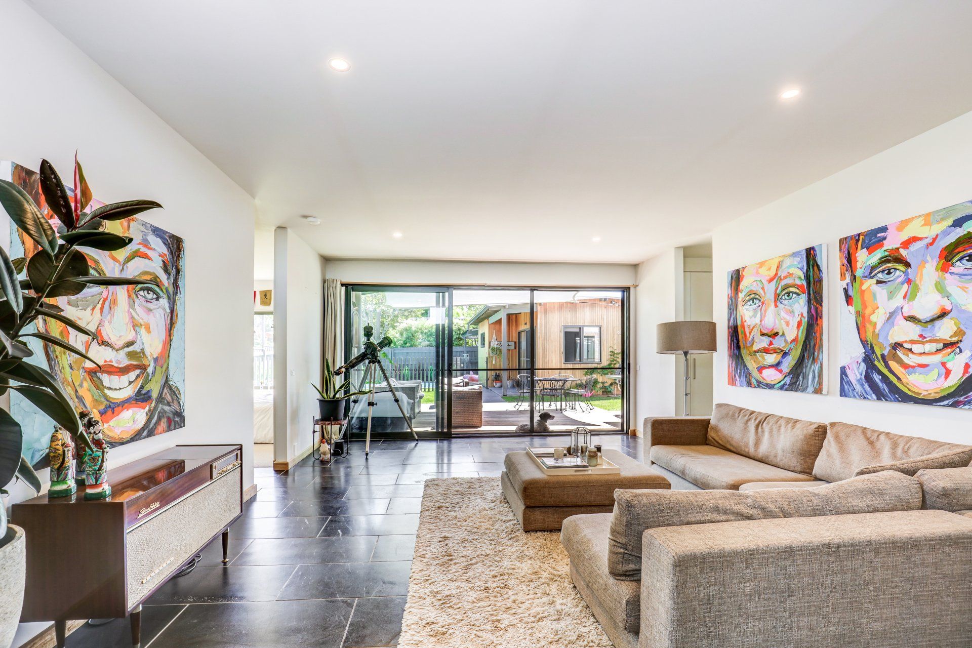 Bright modern living room with beige sectional, colorful portrait art, and sliding doors to a patio