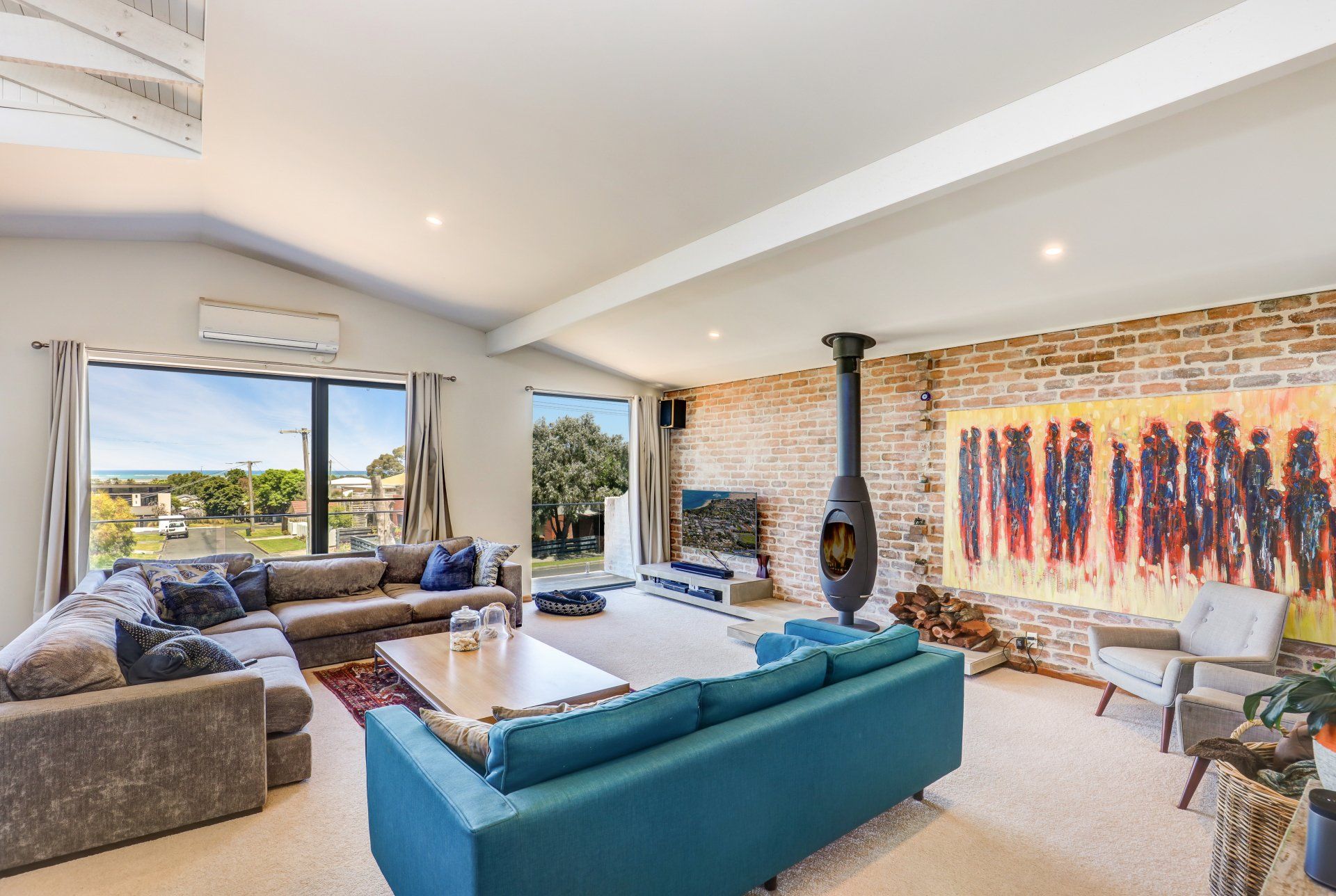 Bright modern living room with teal sofa, fireplace, large windows, and colorful wall art