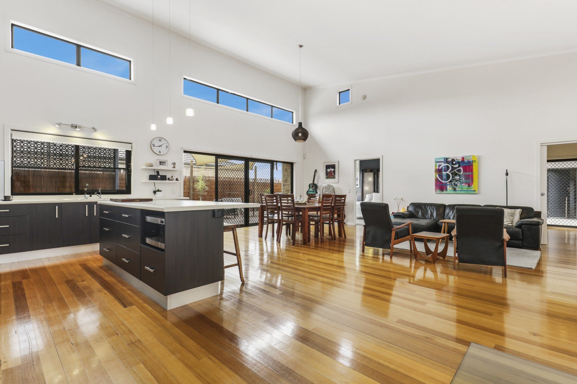 Spacious modern kitchen and living area with polished wood floors, dark cabinets, and dining furniture.