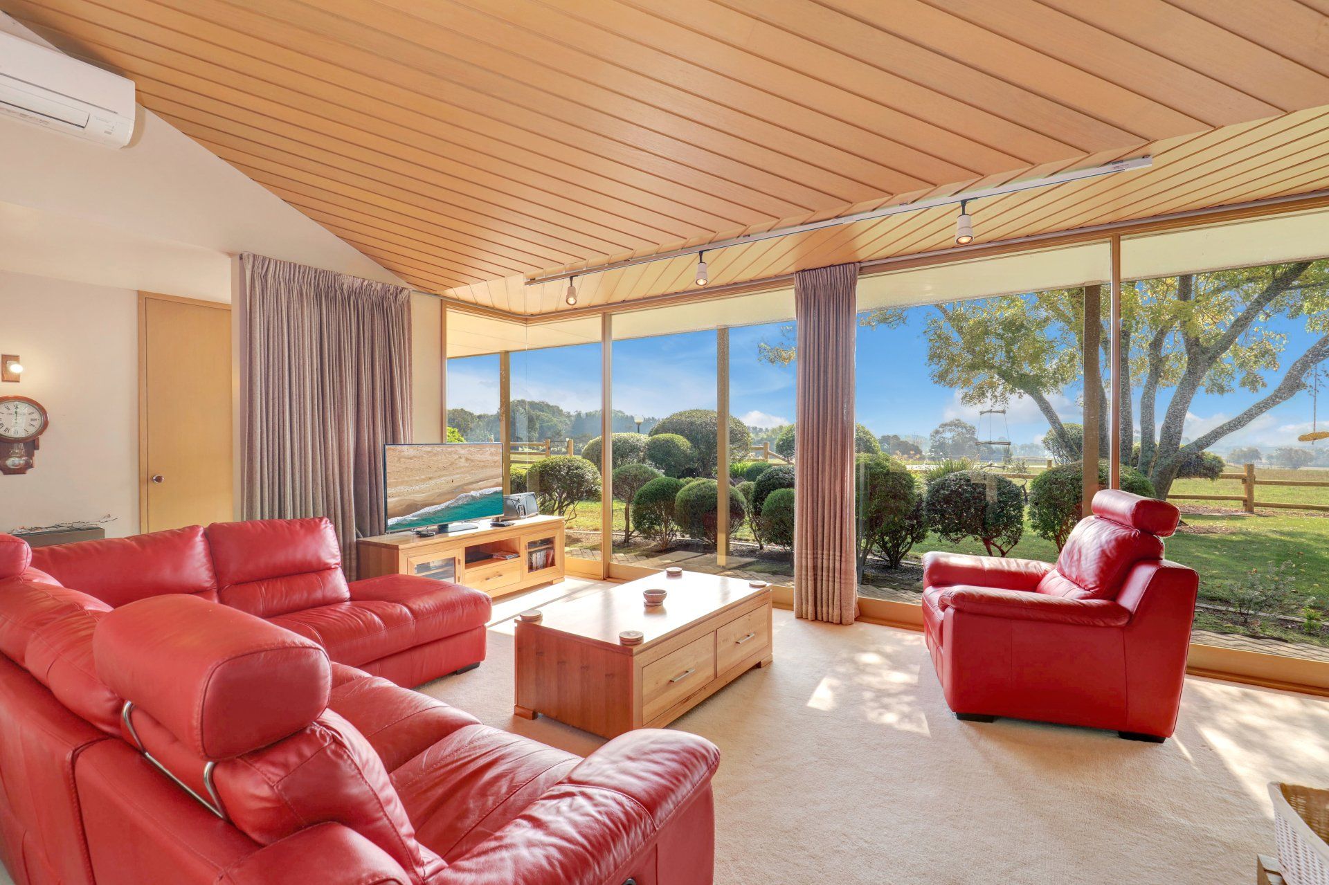 Bright living room with red leather sofas and large windows overlooking a sunny landscape