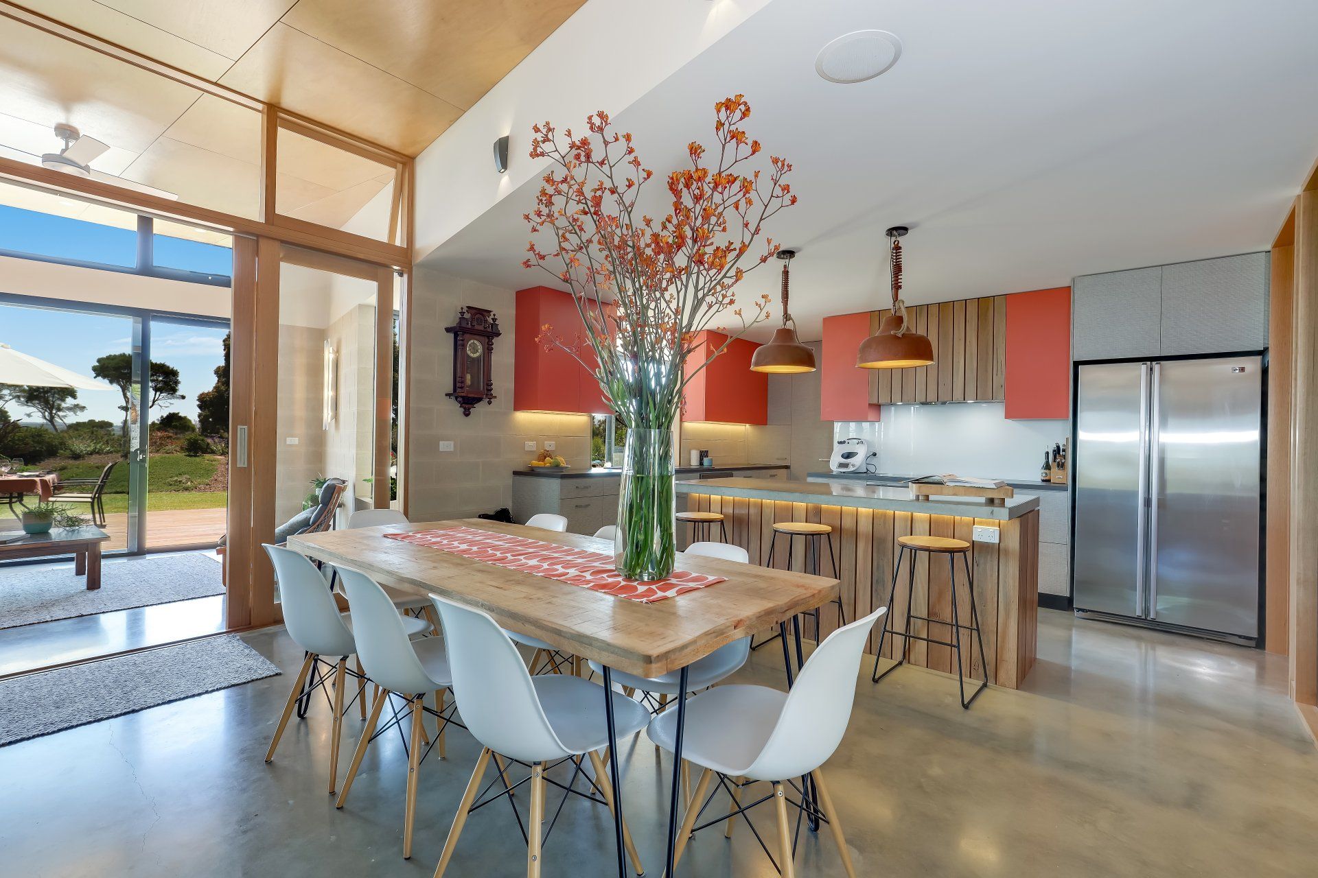Modern kitchen and dining area with large table, white chairs, stainless fridge, and tall window views