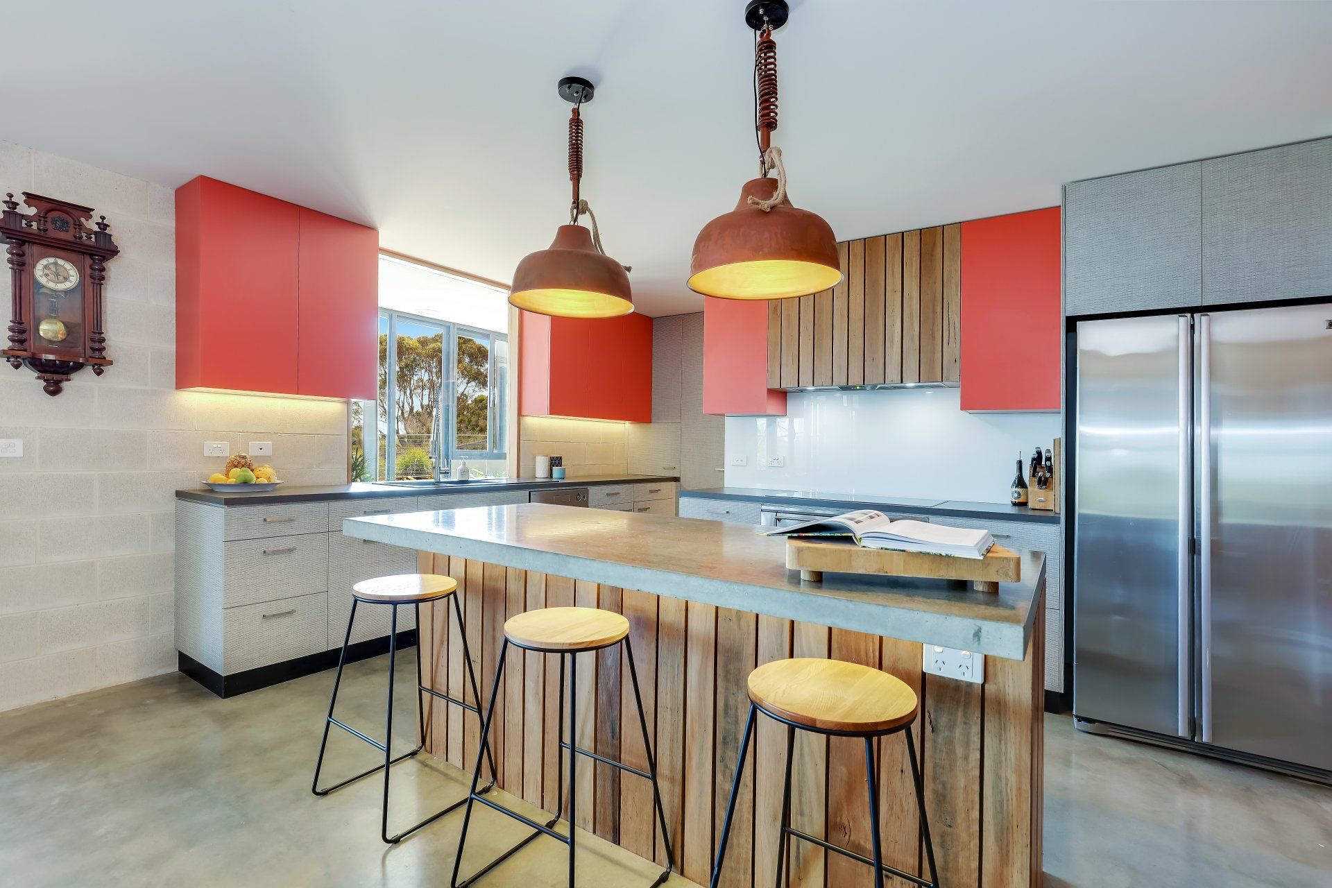 Modern kitchen with red cabinets, island seating, pendant lights, and stainless steel fridge