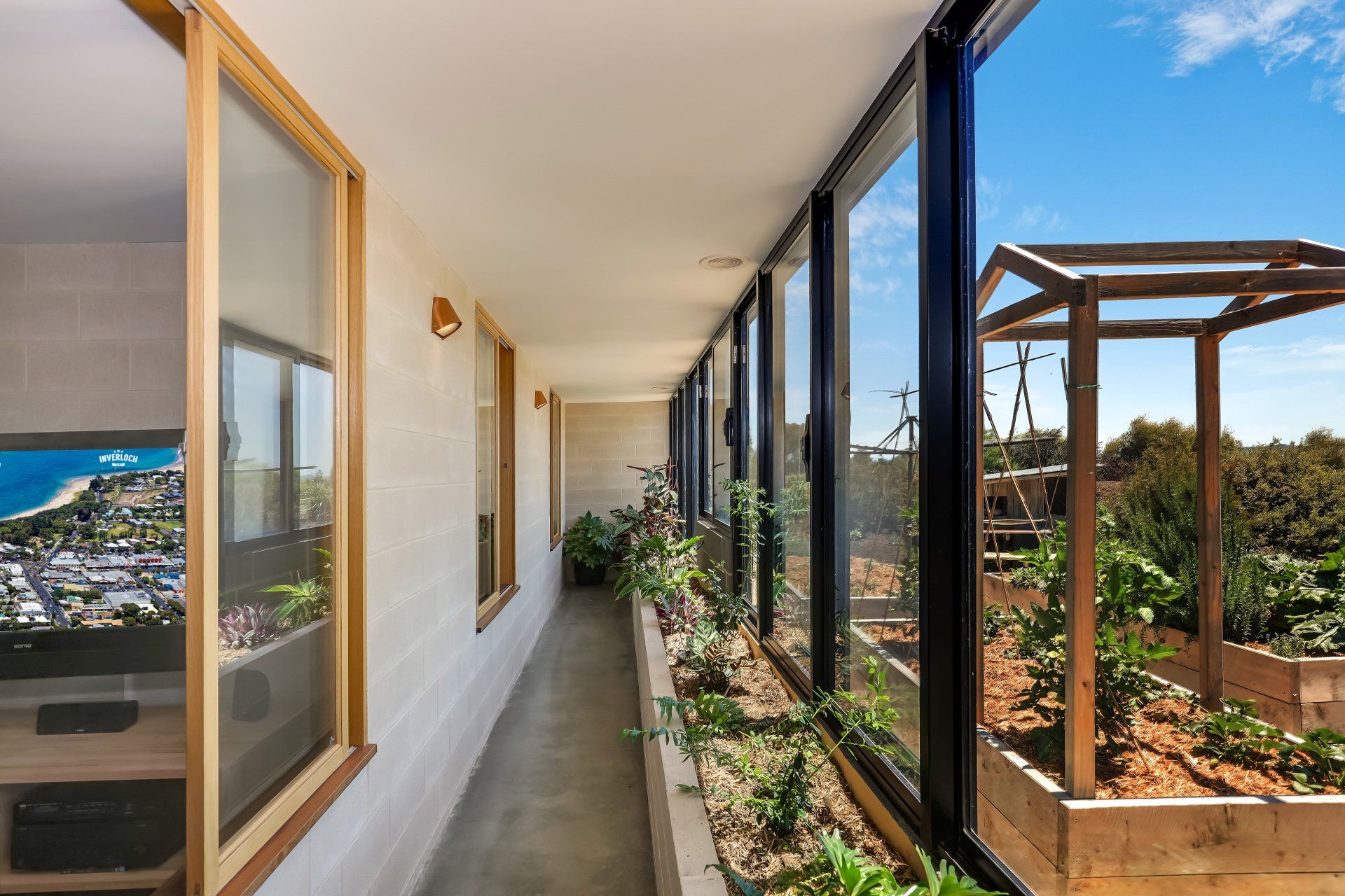 Narrow apartment balcony with potted plants, glass windows, and a sunny outdoor view of hills and buildings