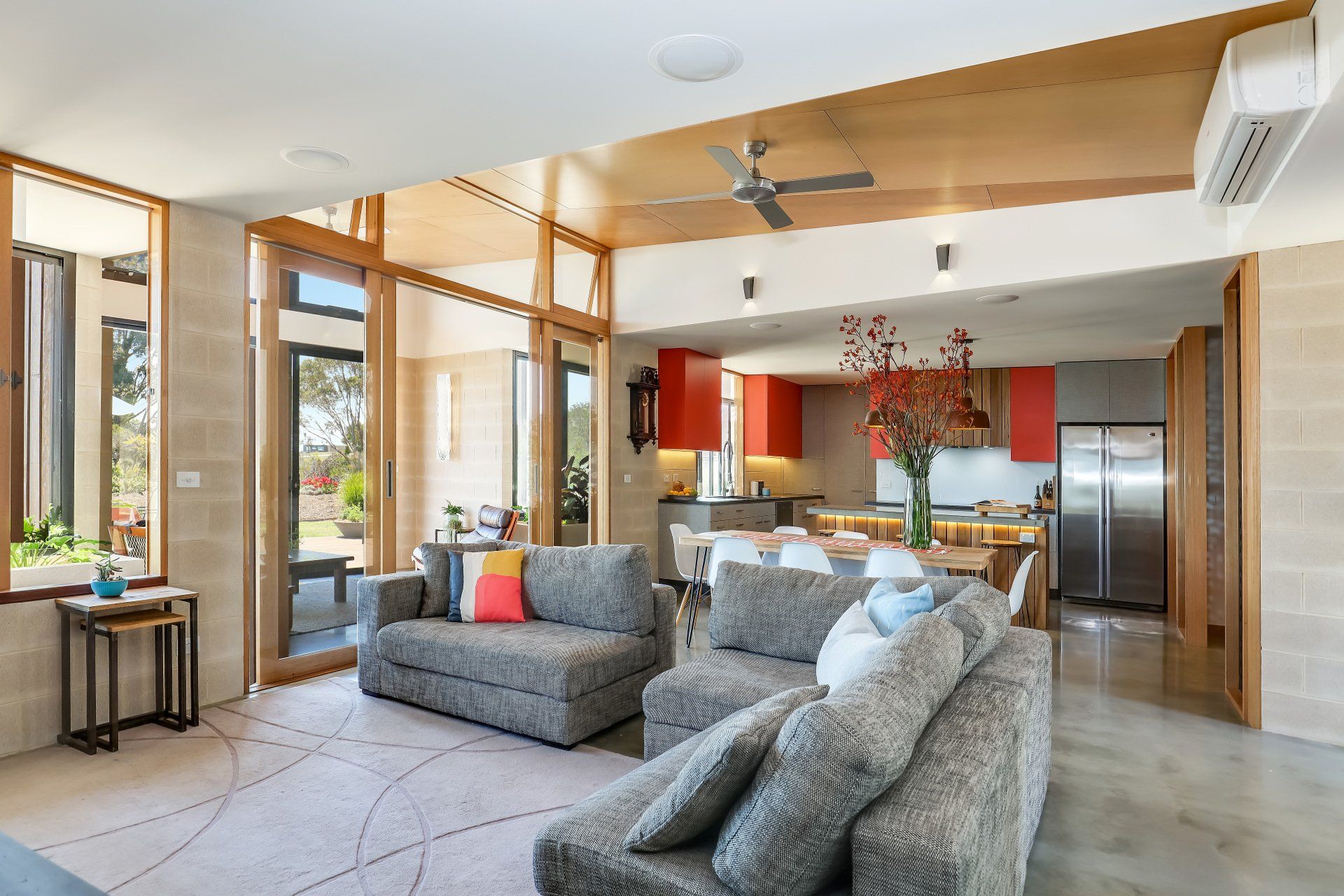 Bright open-plan living room with gray sofas, wood beams, and a modern kitchen in the background