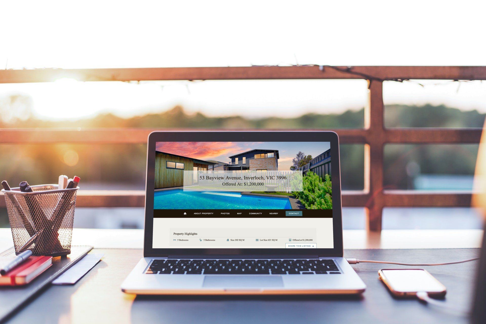 Laptop on a desk by a window, showing a website at sunset with a notebook and phone nearby