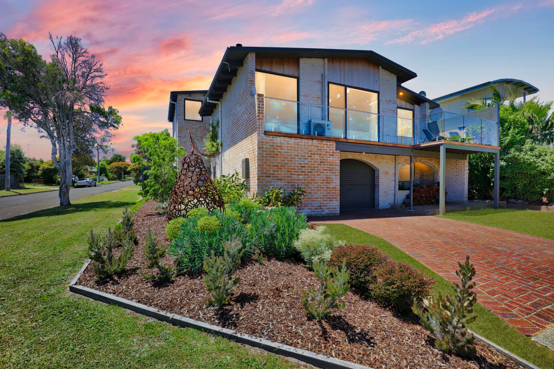 Modern two-story house with stone facade, lit windows, and landscaped front yard at sunset