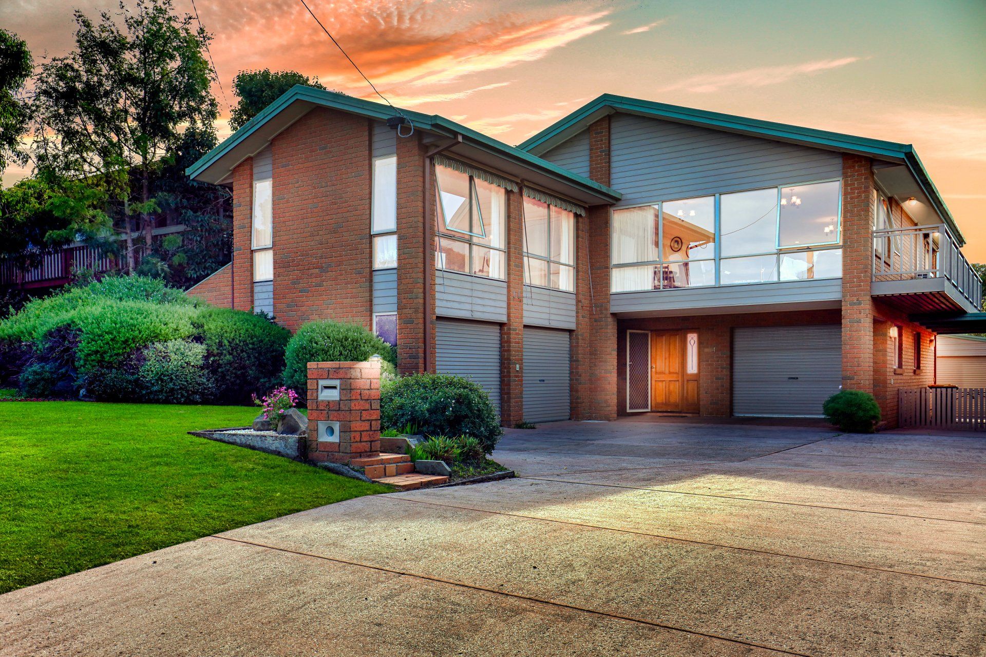 Suburban brick house with a driveway, front lawn, and sunset sky