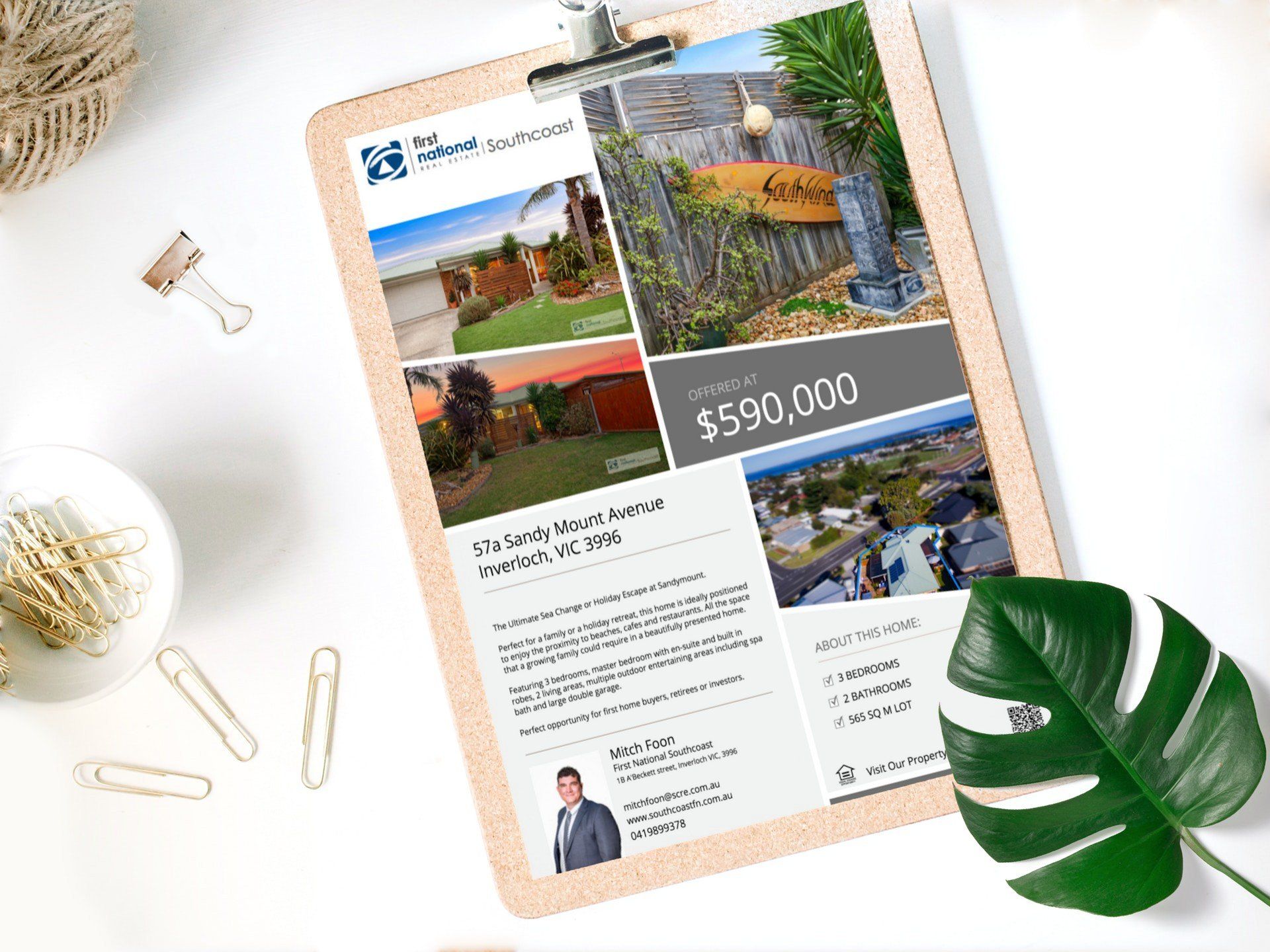 Real estate flyer with home photos, $599,000 price, on a clipboard beside a green leaf on a white desk