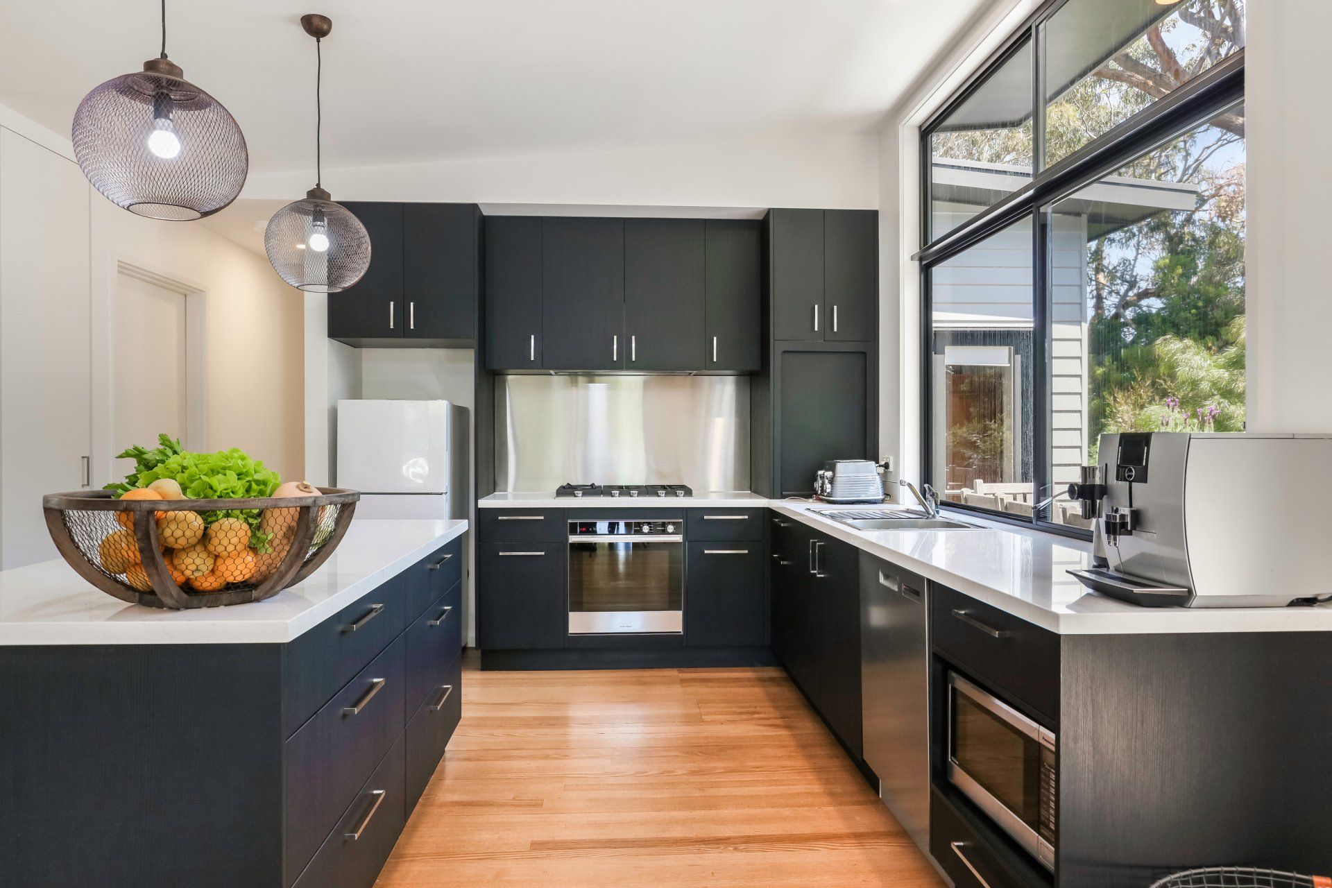 Modern black-and-white kitchen with island, large windows, stainless appliances, and wood floors