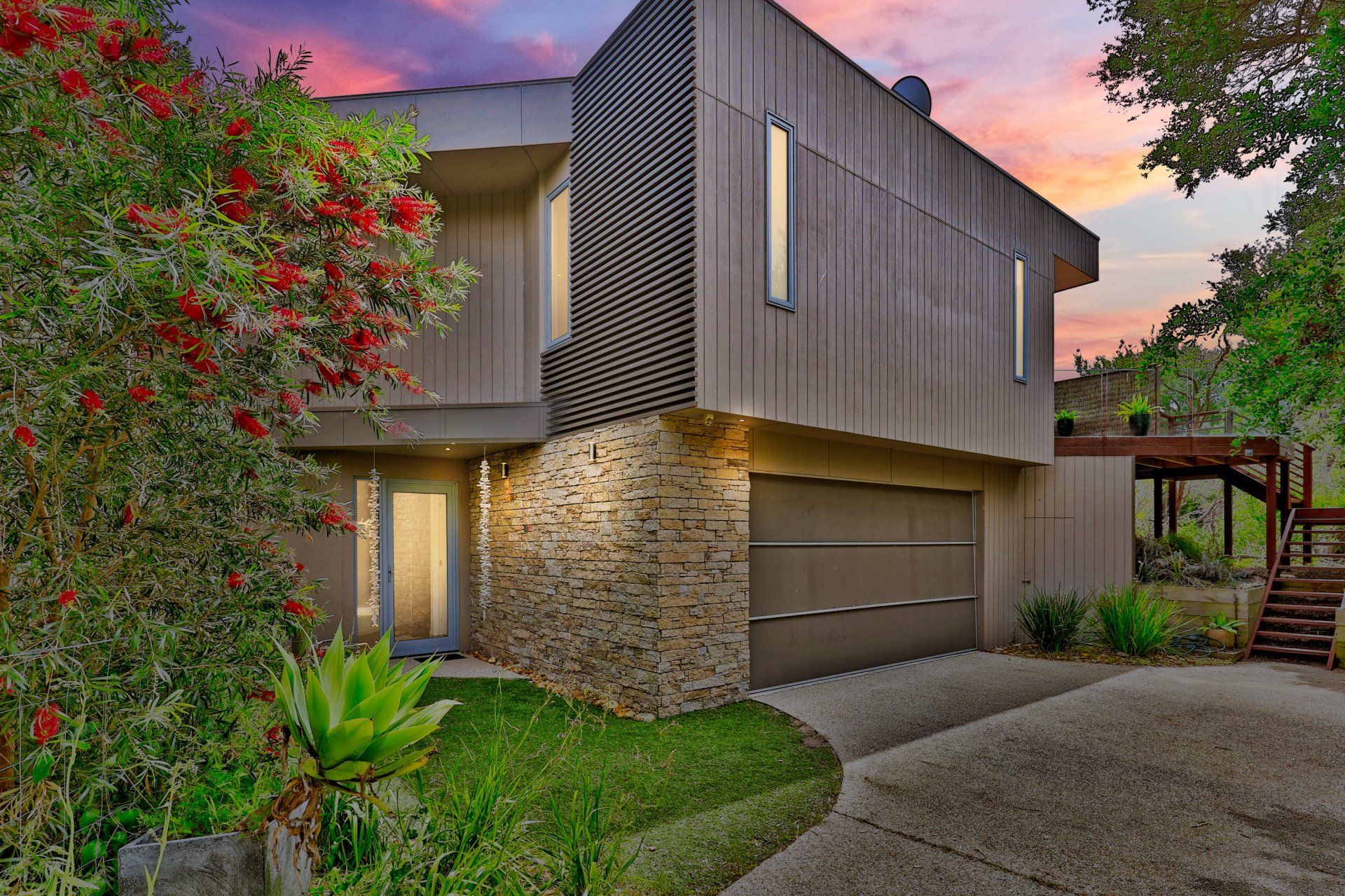 Modern two-story house with stone facade, garage, and lush front yard at sunset