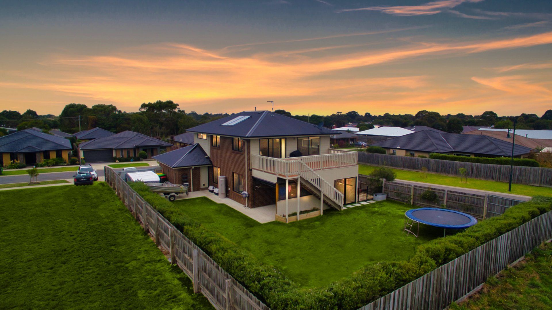 Suburban house with green lawn and fenced yard at sunset